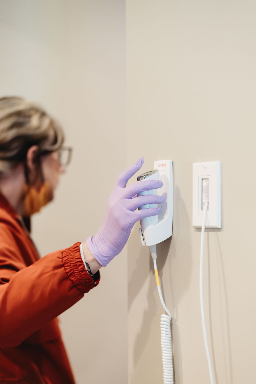 Person wearing protective gloves cleaning electrical outlets on a white wall.