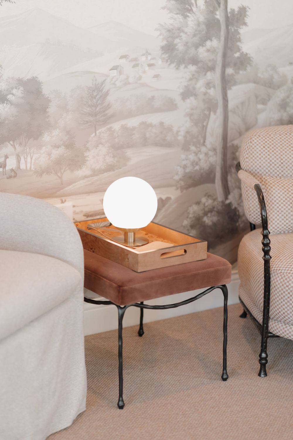 Modern bedside table with spherical white lamp and black metal legs against a mural wallpaper background.