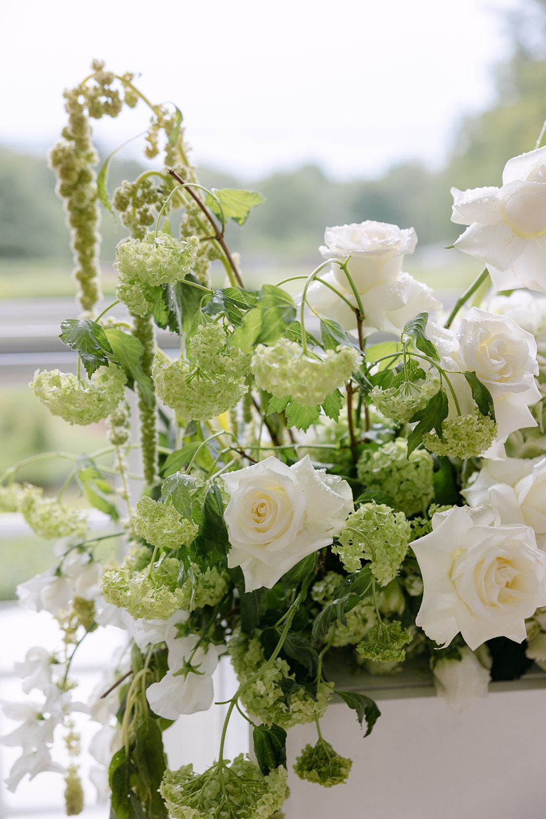 Elegant white roses and green viburnum flowers arranged in a soft, romantic floral centerpiece display.