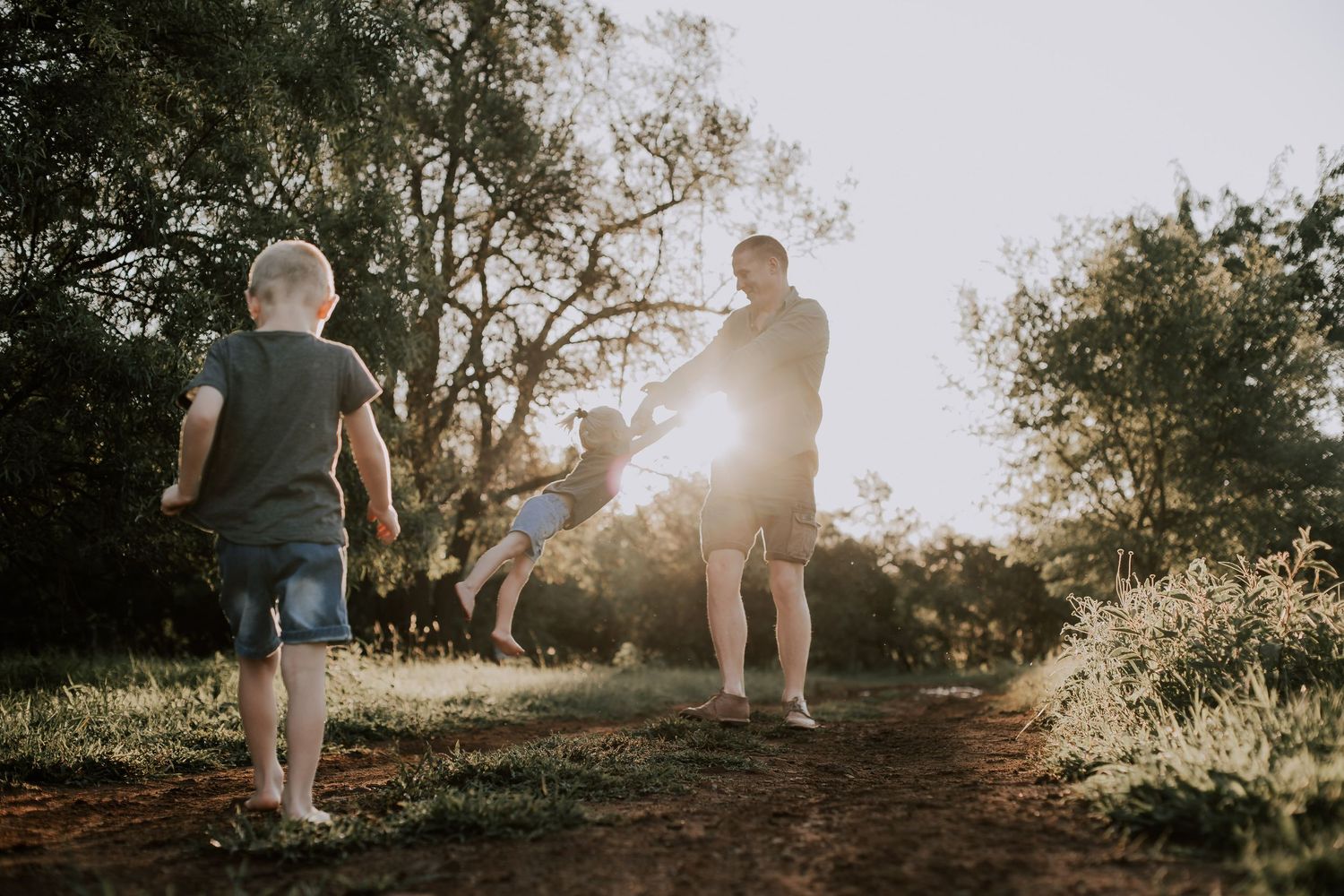 A series of silhouetted figures walking along a sunlit nature trail during golden hour.
