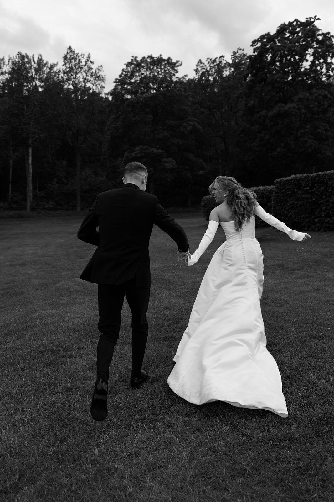 A sequence of black and white photos shows a couple in wedding attire playfully running across a grassy field.