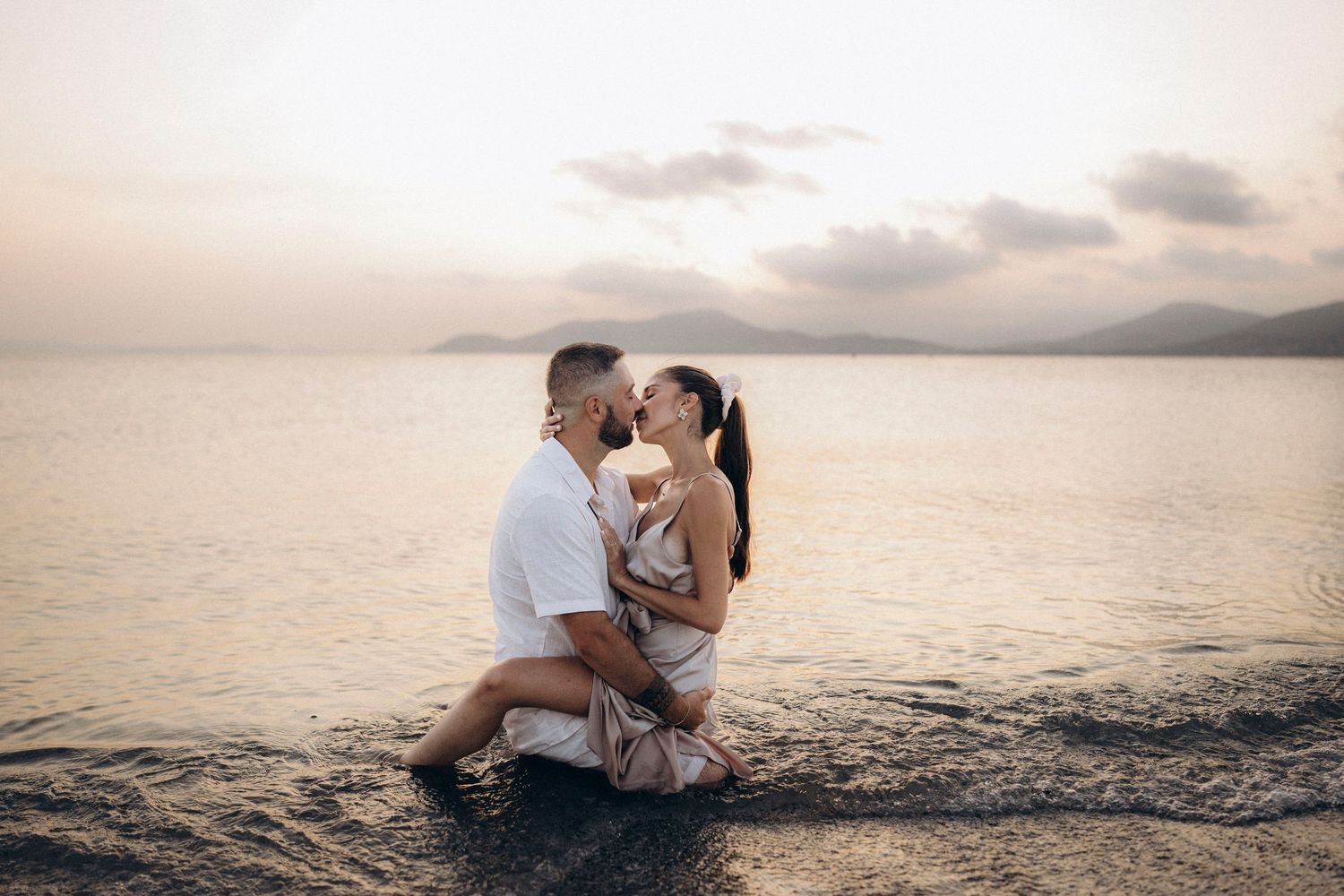 A romantic beach photoshoot silhouette at sunset shows a couple embracing by the ocean waves.