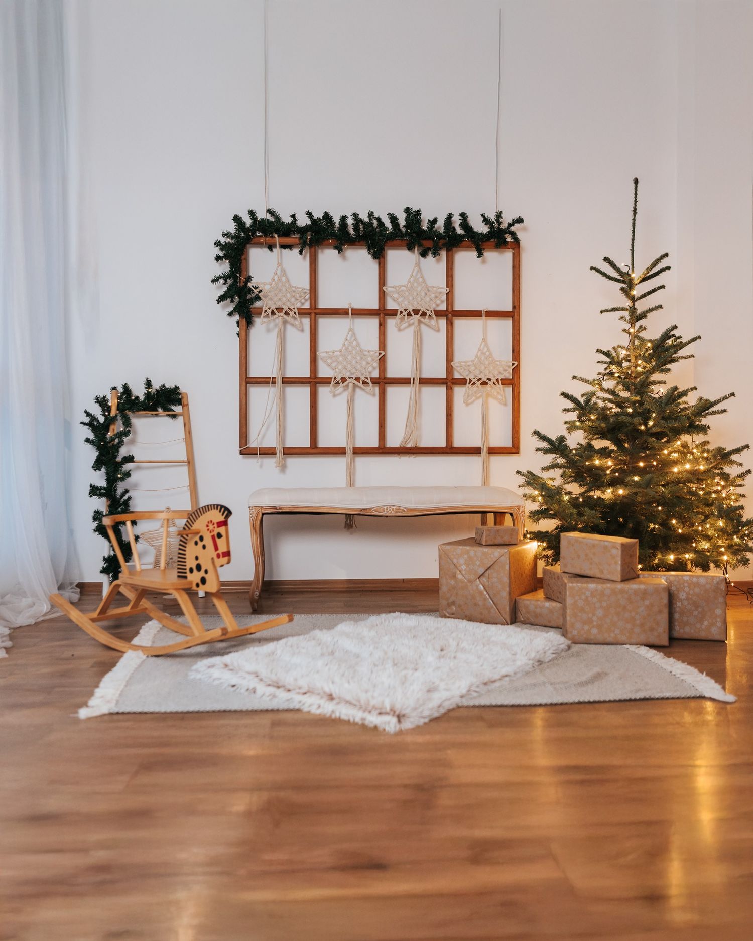 A wooden rocking horse sits in a cozy room decorated for Christmas with a tree and wall decor in warm lighting.