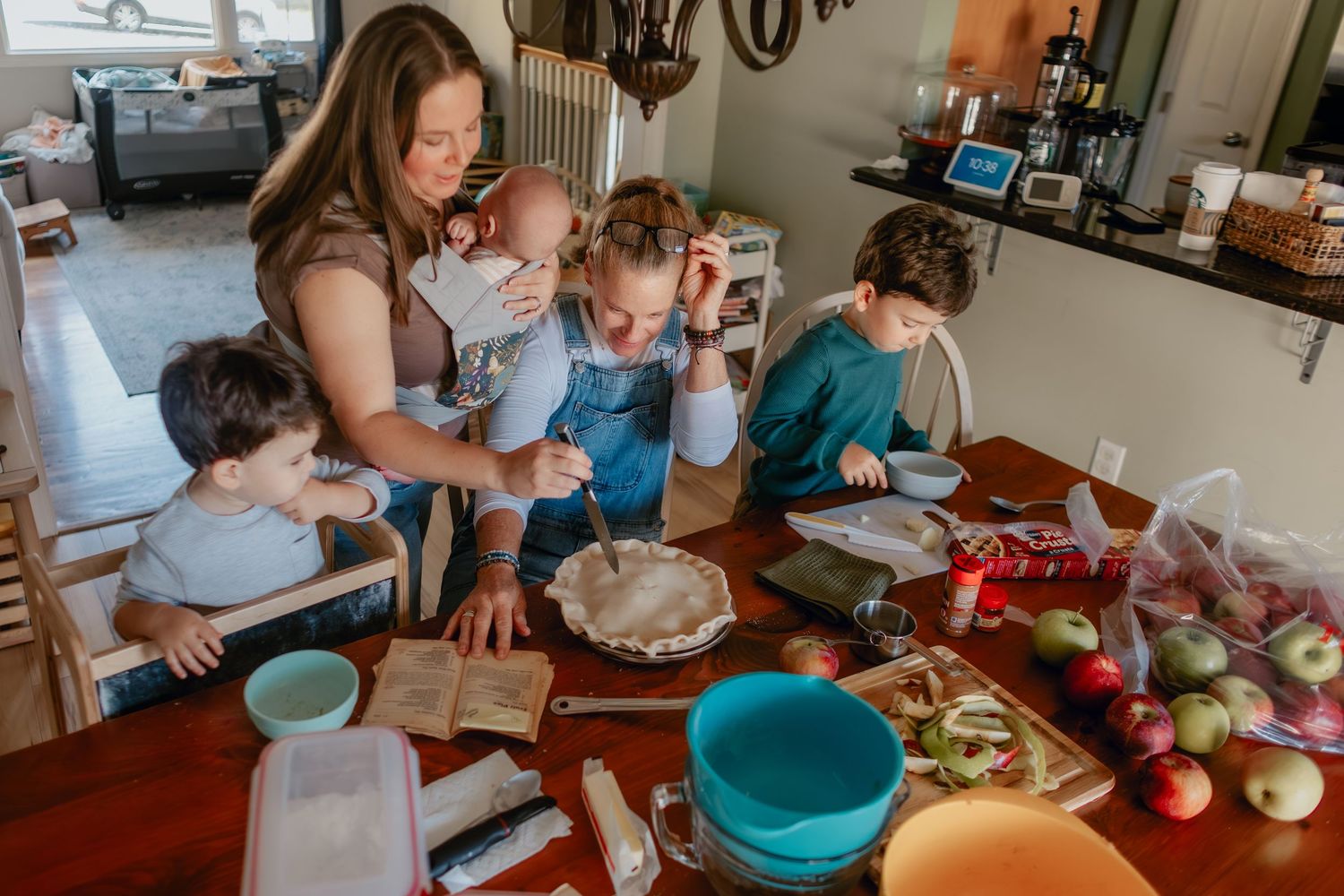 A group gathers around a kitchen counter preparing food together with colorful bowls and ingredients spread across the surface.