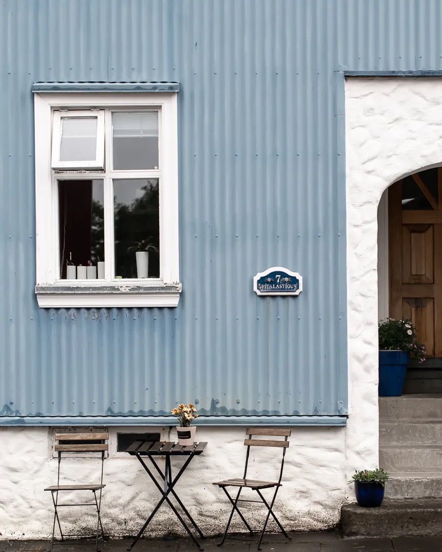 Blue house exterior with a white window, small sign, and a single chair outside.