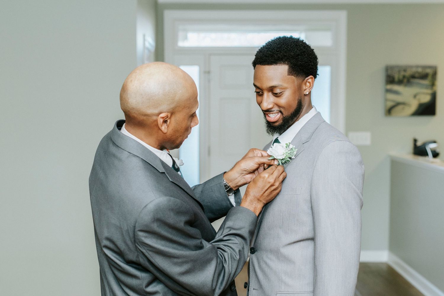 Two people in formal gray suits embrace in an emotional moment during what appears to be a wedding ceremony.
