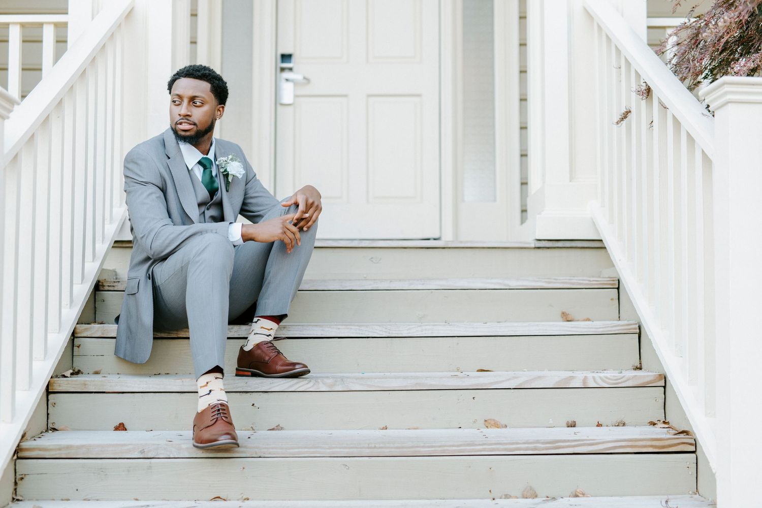 A couple sits on white porch steps during an outdoor engagement photo session.