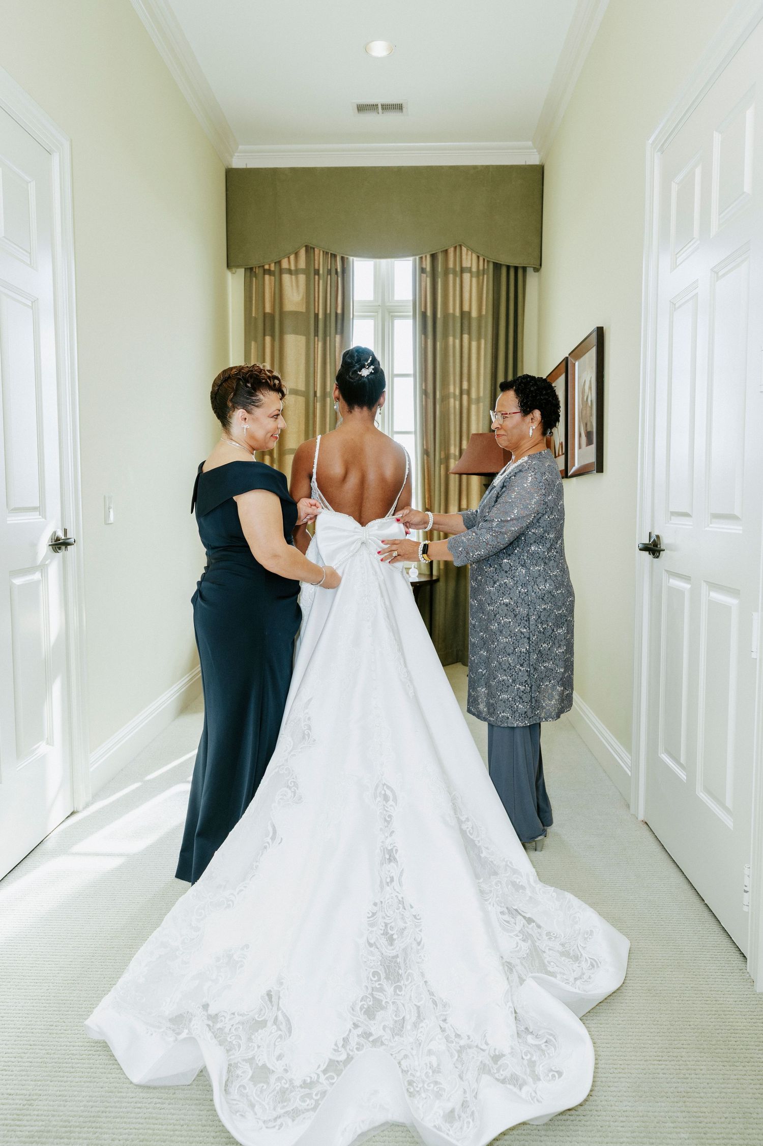 Behind-the-scenes wedding preparation showing bride getting dressed with help in a bright hallway.