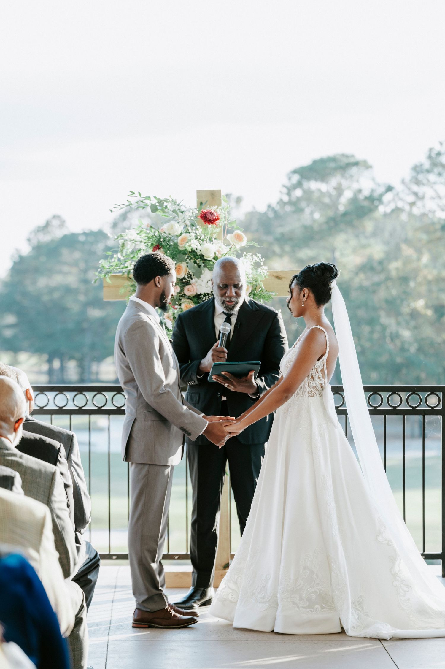 Wedding ceremony taking place on a scenic waterfront balcony with elegant white decor and floral arrangements.