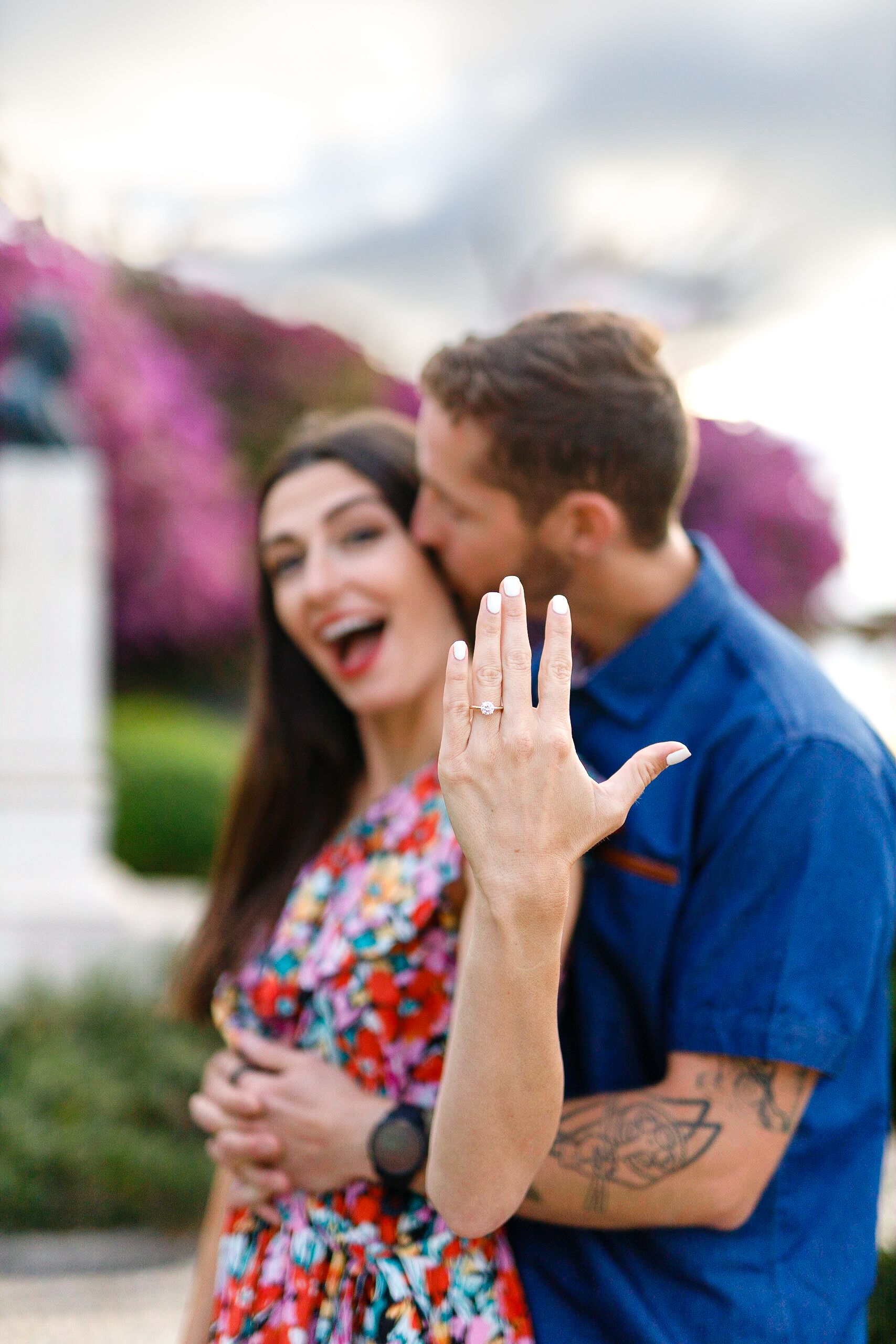 A couple shares a joyful moment together outdoors while showing off a new engagement ring.
