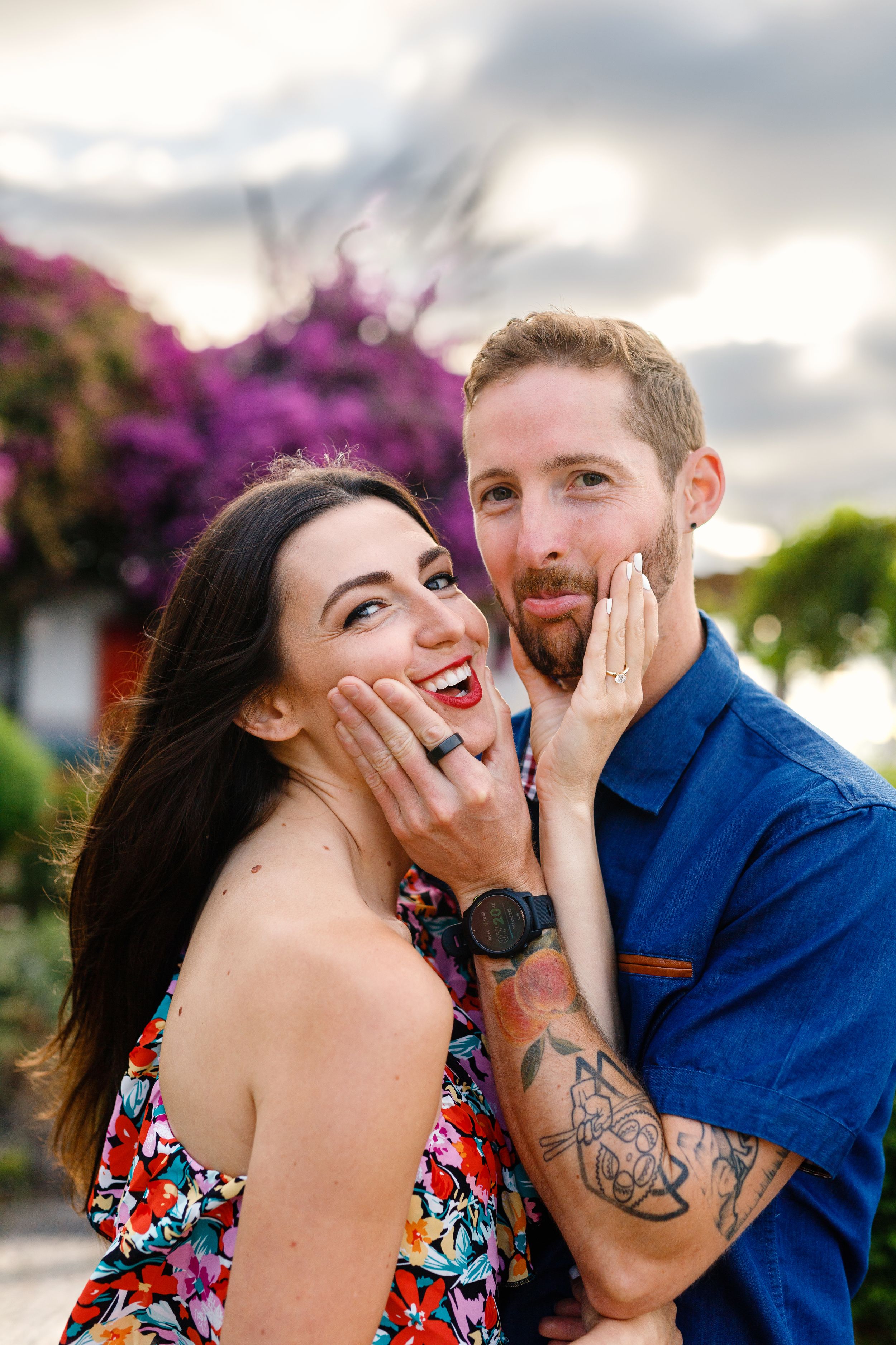 A joyful couple shares a playful moment together with bright purple flowers in the background.