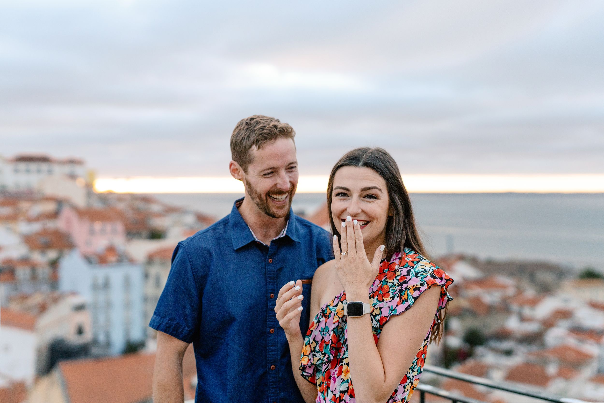 A couple laughs together while enjoying a scenic view of coastal buildings at sunset.