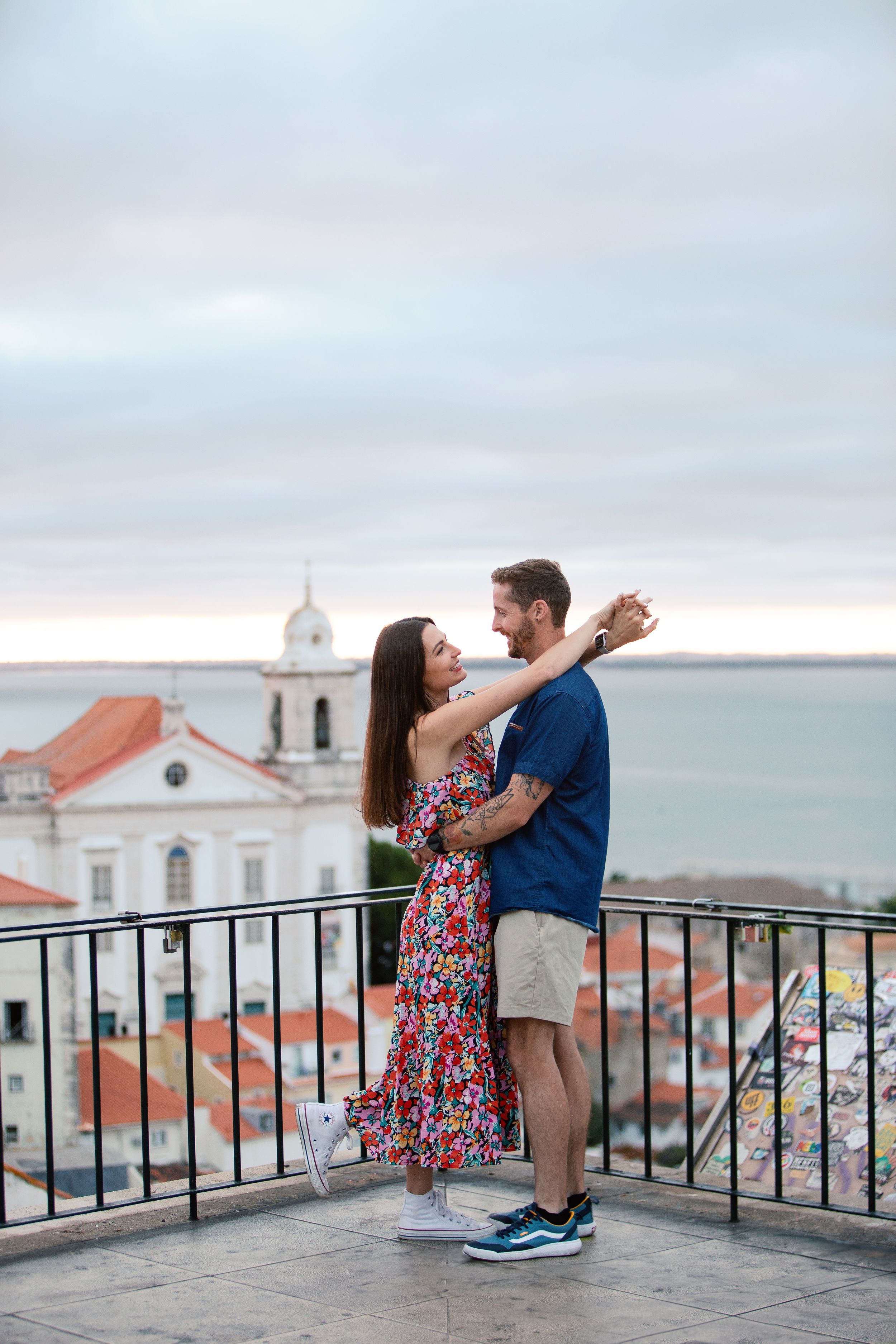 Romantic couple sharing intimate moments on a scenic overlook with white church and coastal town views.