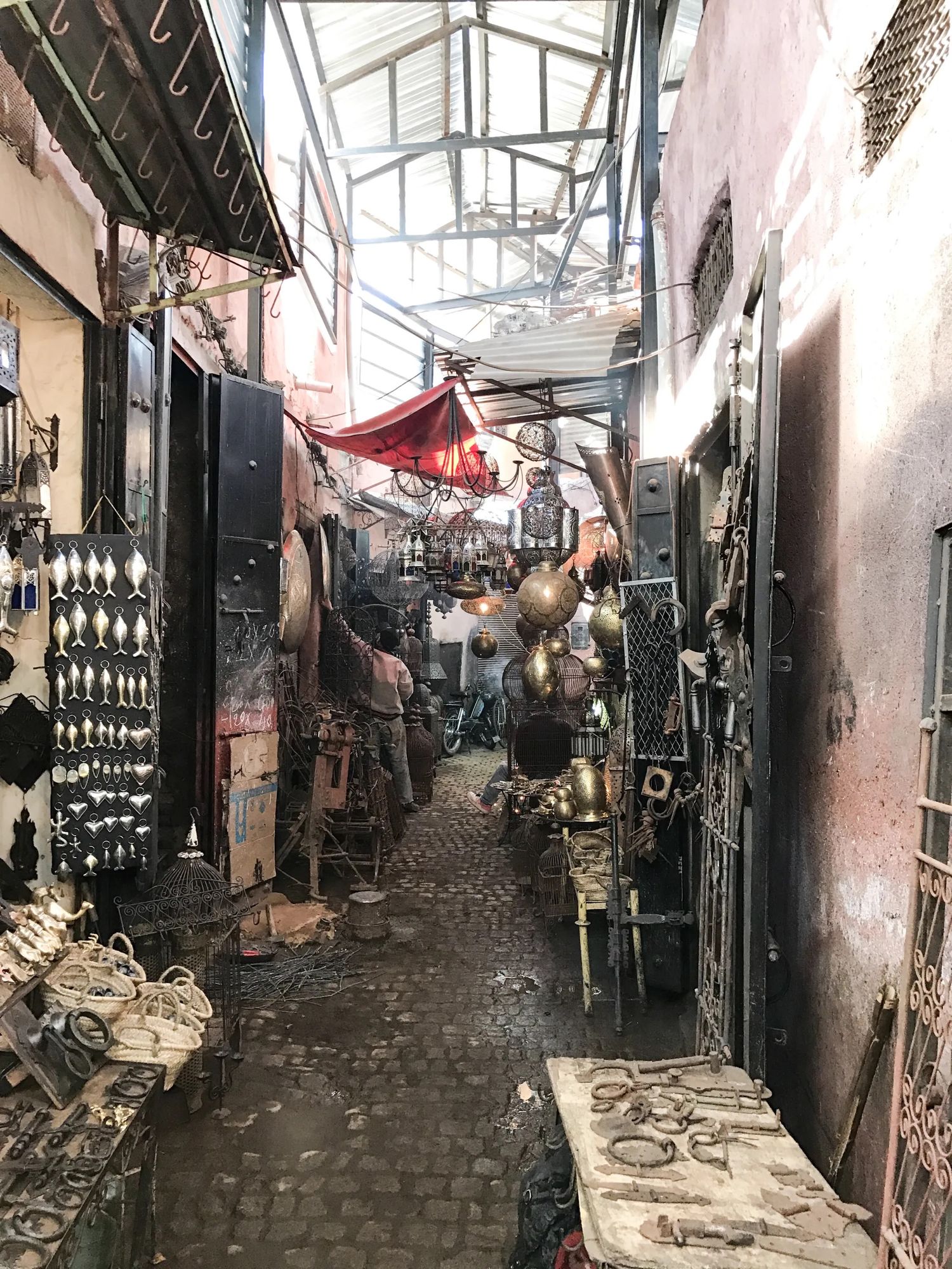 A narrow, crowded Moroccan market alley lined with stalls, textiles and street vendors.