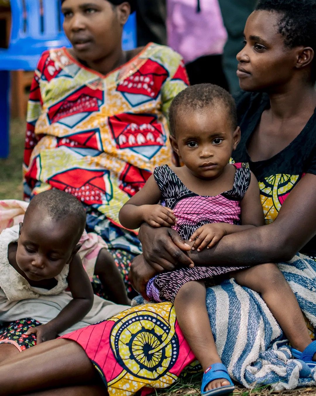Women sit together holding babies and young children, showing family life, community support and caregiving.