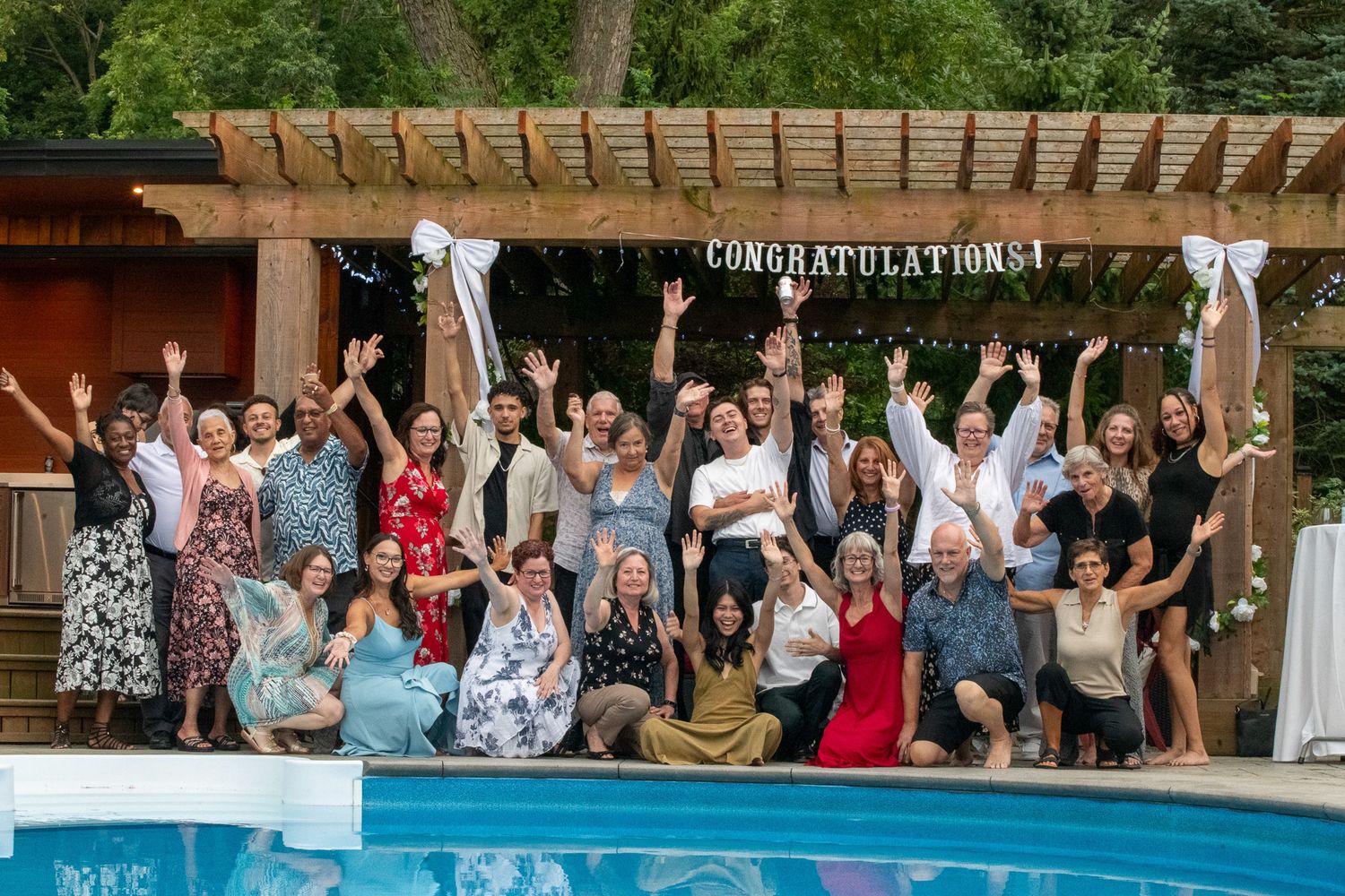 Taken in Jordan, Ontario while a large wedding group celebrates at an outdoor party under a wooden pergola next to a swimming pool.