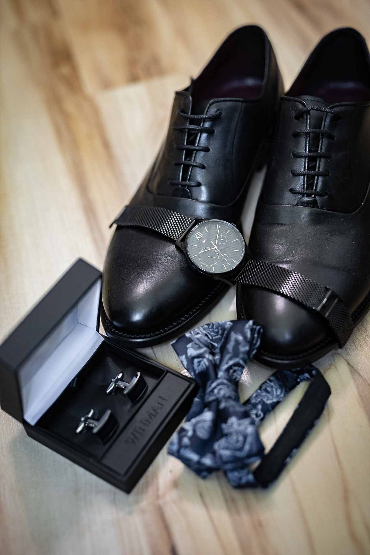 Black leather dress shoes with navy socks and accessories arranged on a light surface.