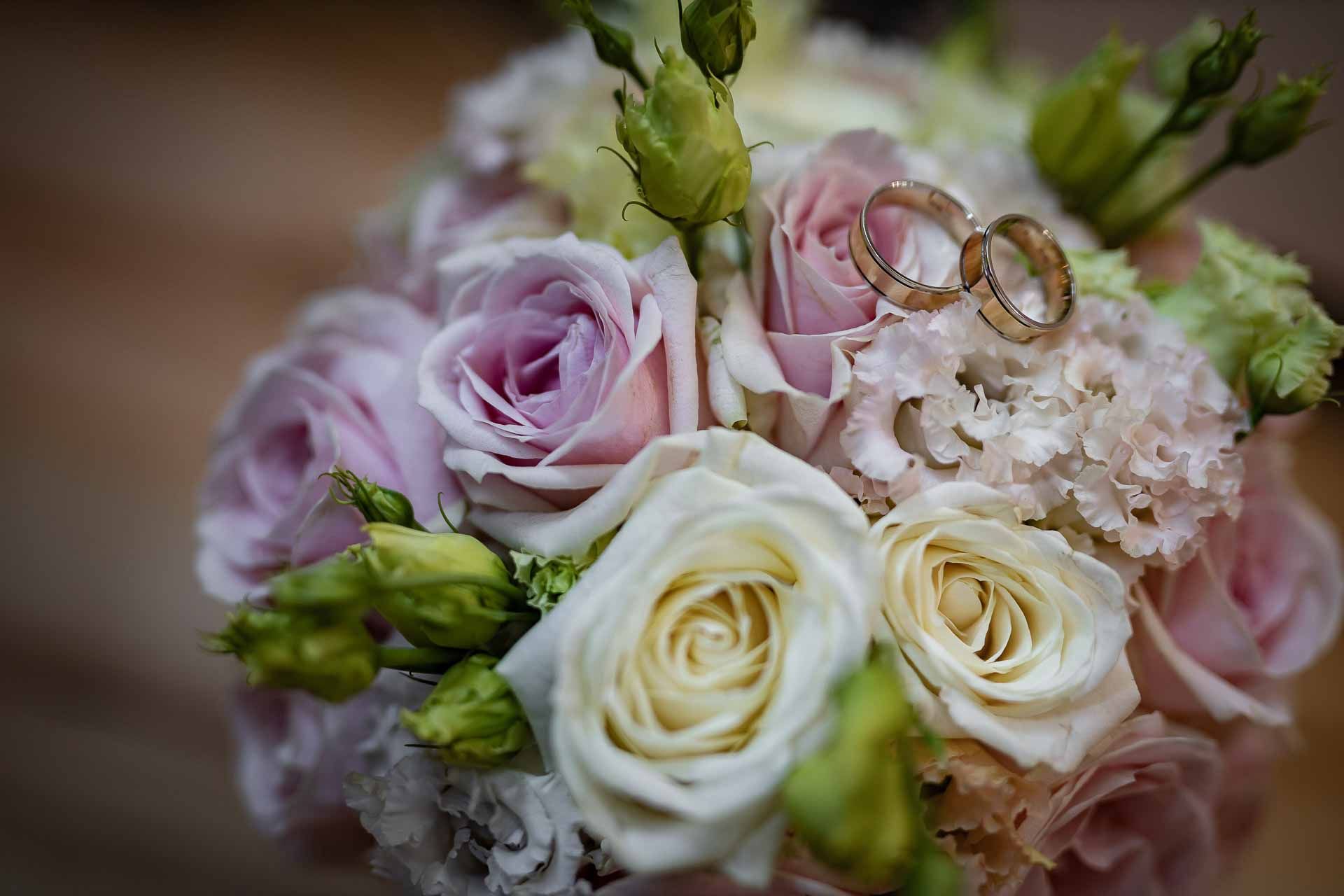 Wedding rings nestled among pink and white roses in a bridal bouquet.