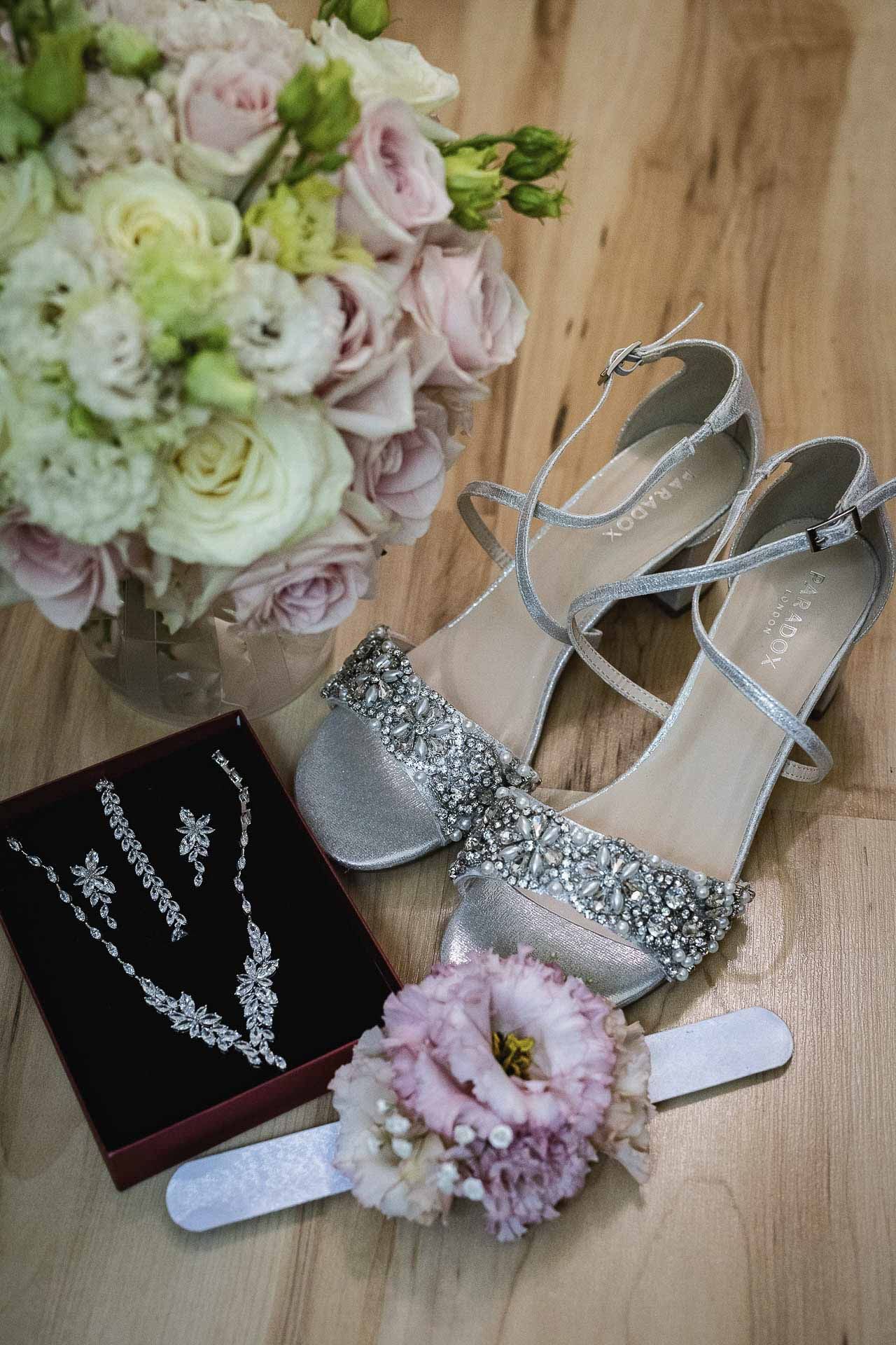 Elegant silver bridal shoes with crystal details alongside jewelry and floral accessories.