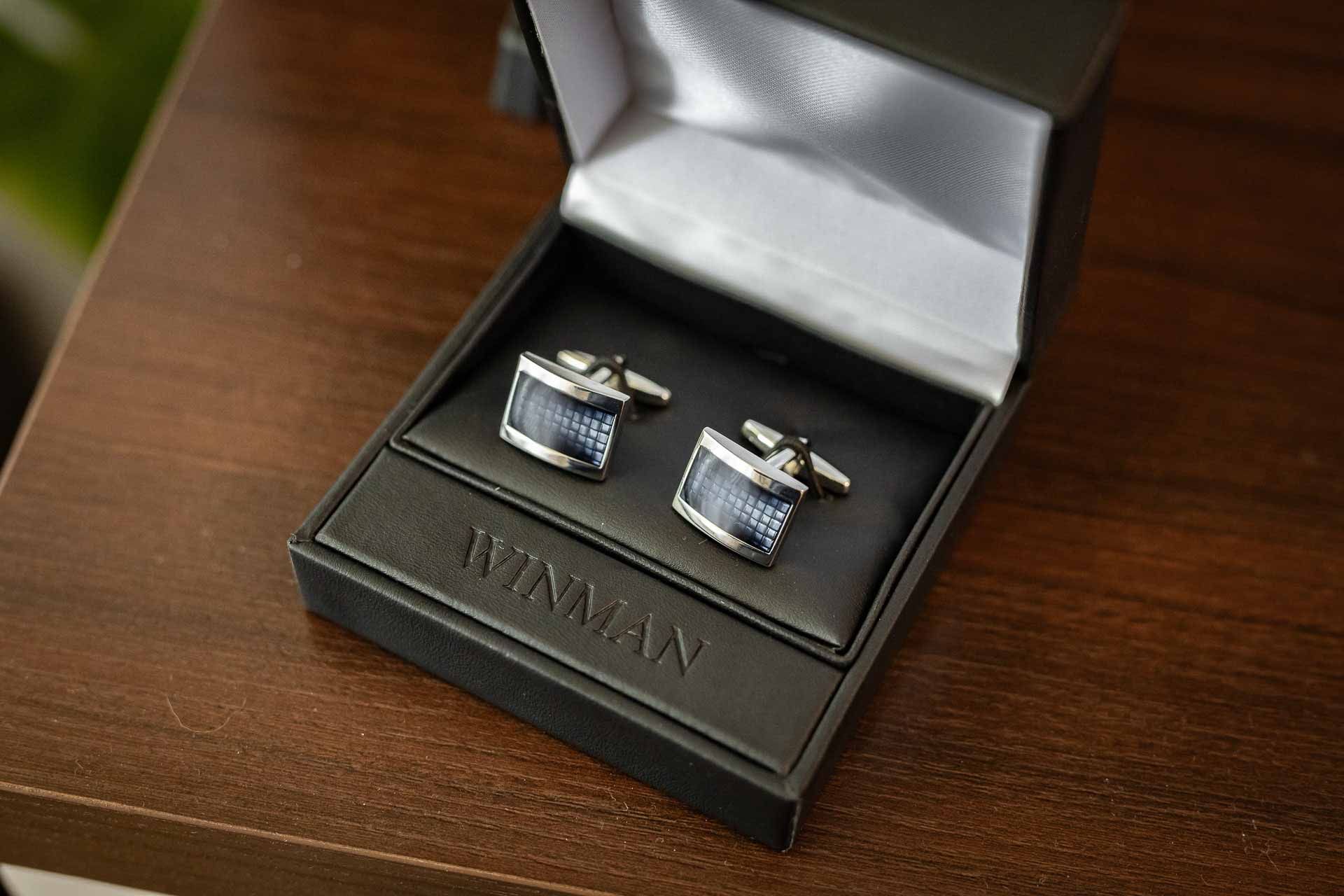Silver cufflinks displayed in black presentation boxes on wooden surface.