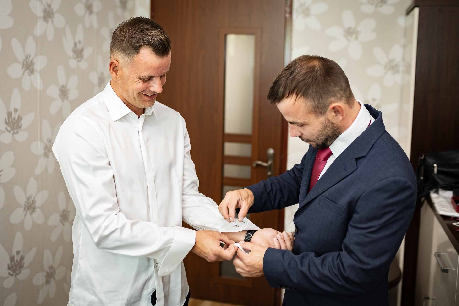 Men in suits adjusting formal attire during wedding preparation.