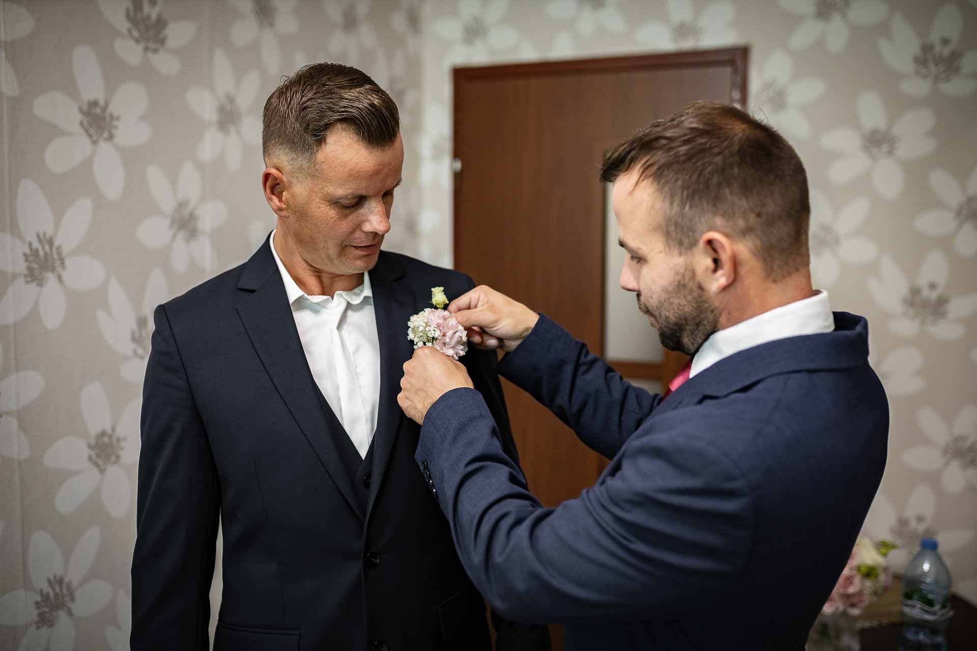 Groomsmen helping with wedding day preparations in formal attire.
