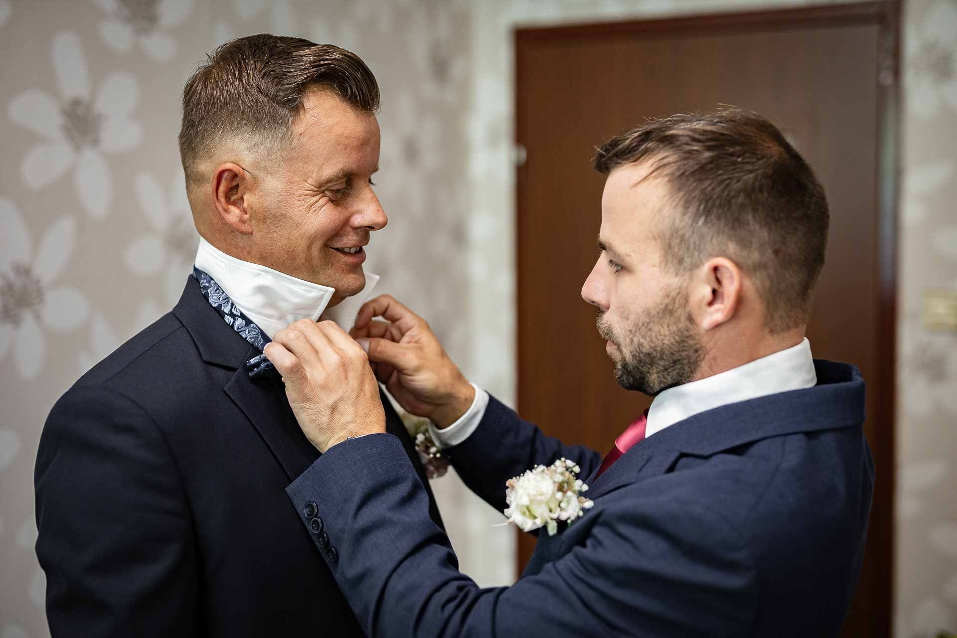 Wedding party members adjusting ties and boutonnieres before ceremony.
