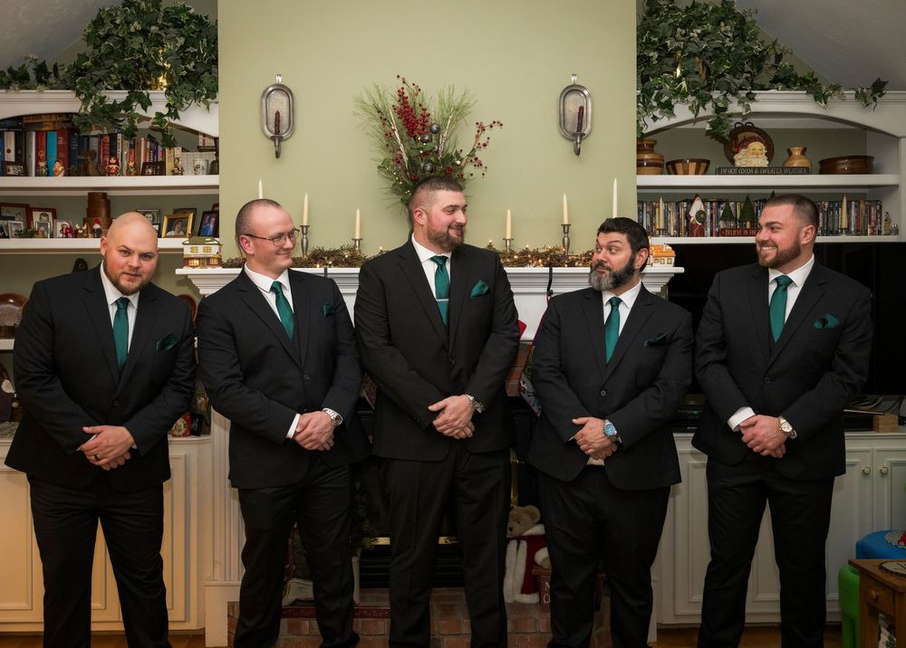 Groomsmen in black suits and teal ties lined up in formal wedding party photo.