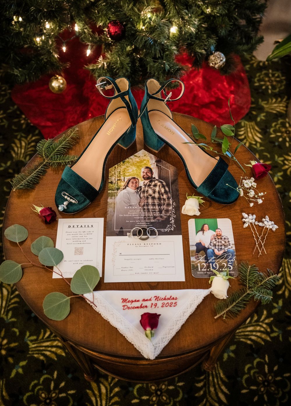 Wedding invitation details and teal high heels arranged with eucalyptus leaves and Christmas decorations on a wooden surface.