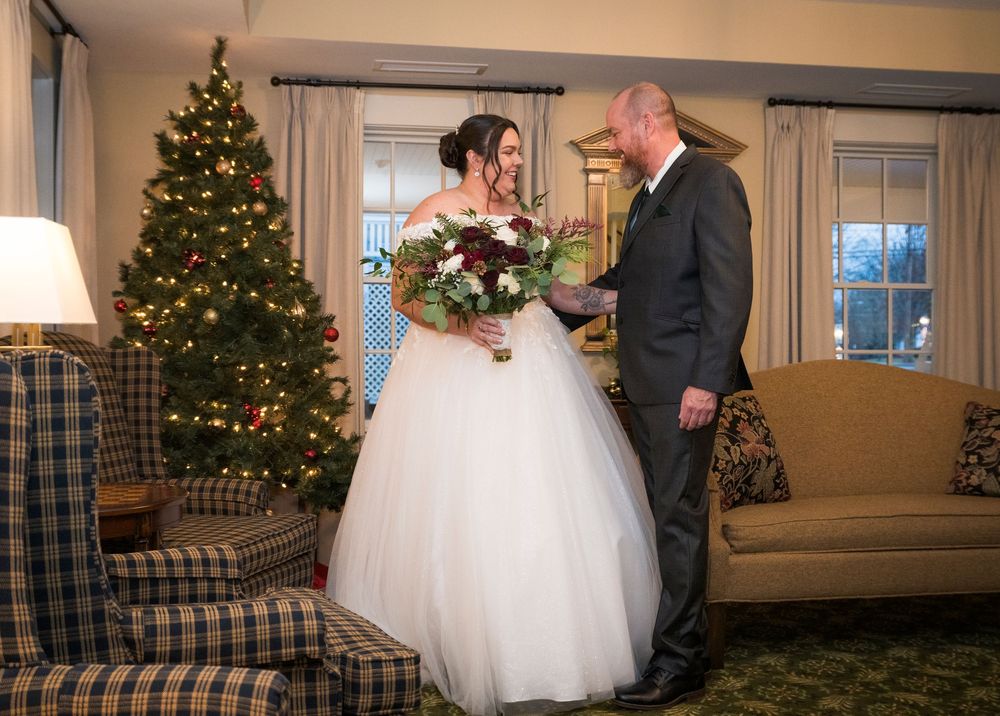 Indoor wedding celebration with Christmas trees and winter decorations visible through windows.