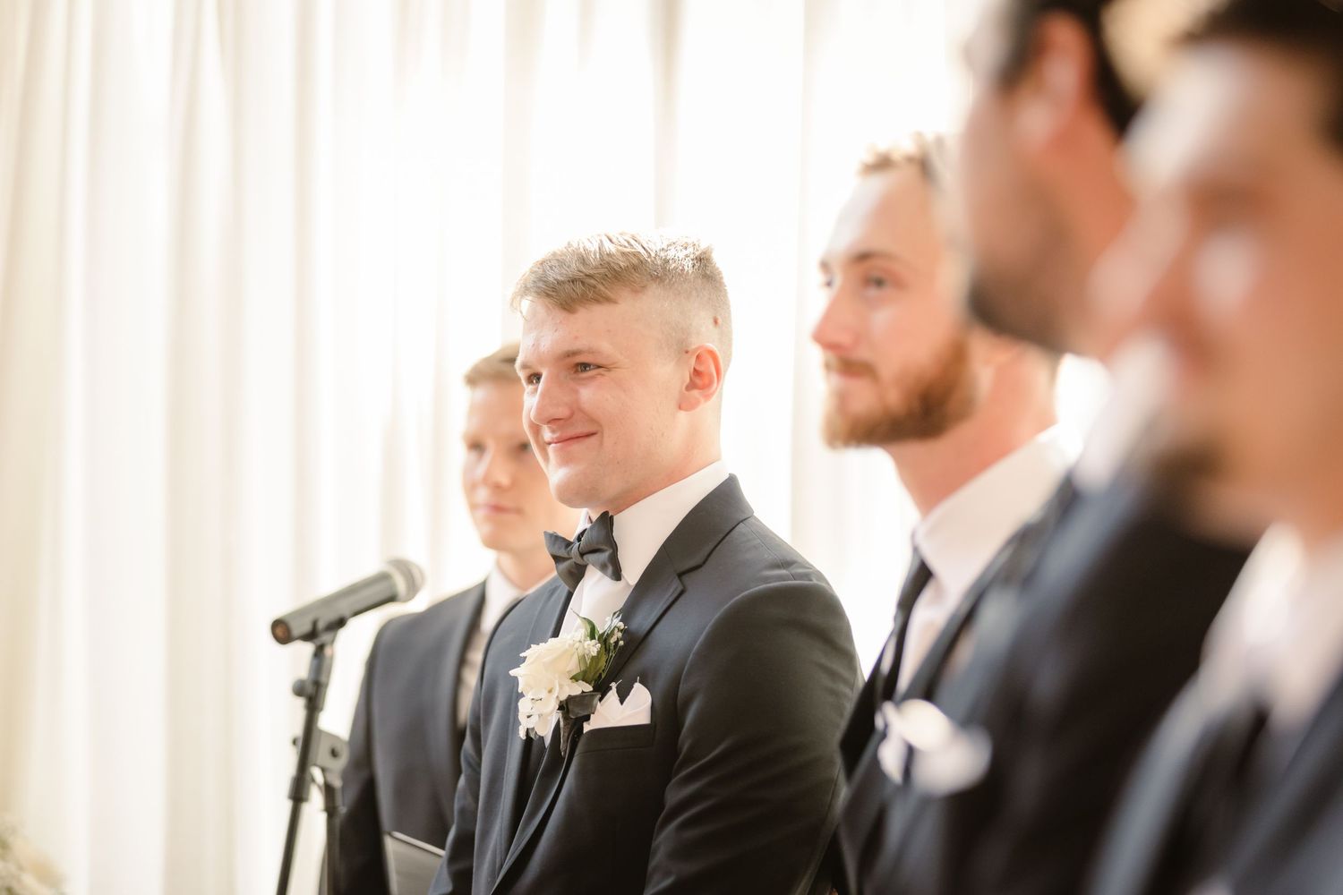 Groomsmen in dark suits and ties share a laugh during a candid moment at a wedding ceremony.