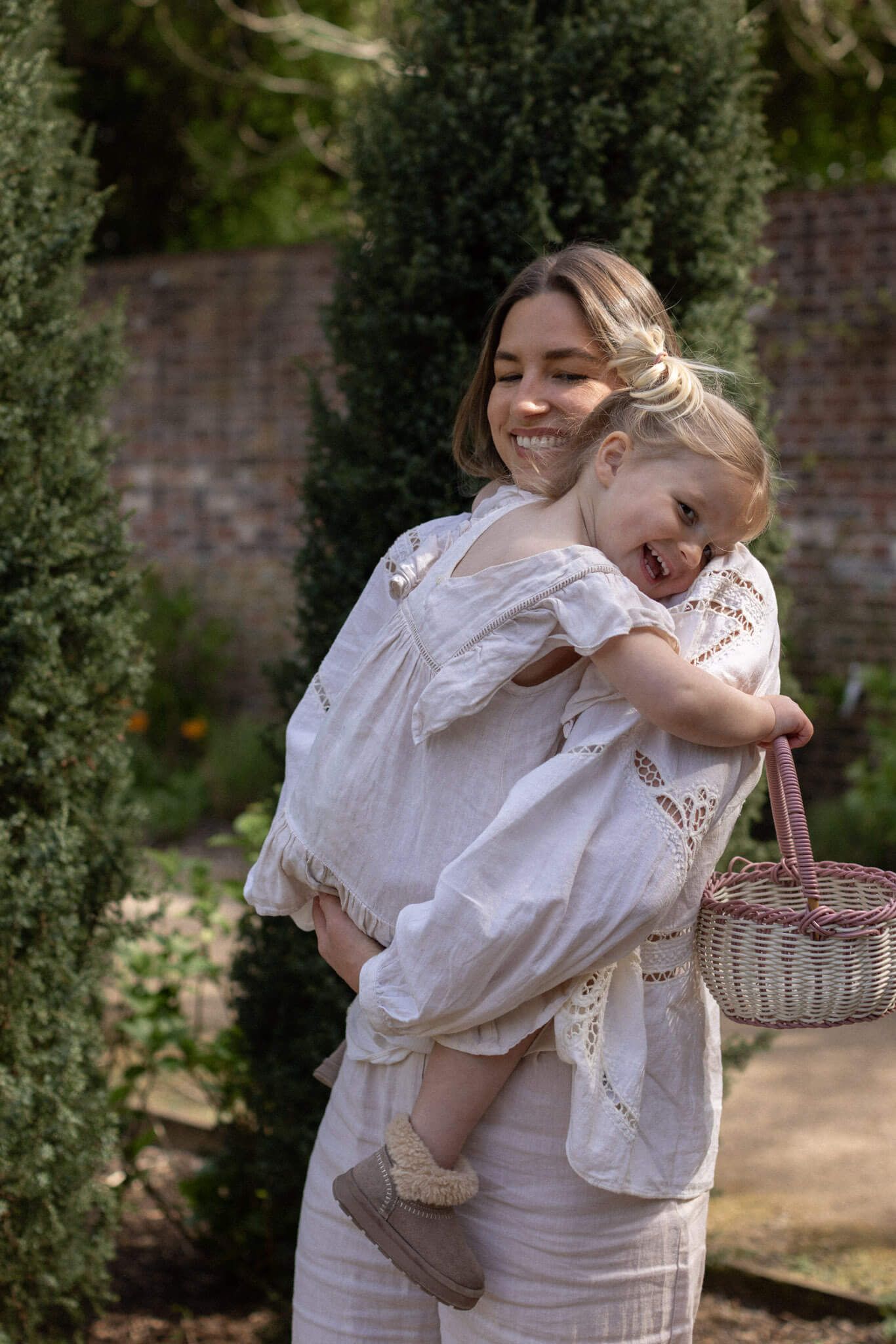 A smiling woman holds a laughing toddler with a wicker basket during a family photography session in Brighton