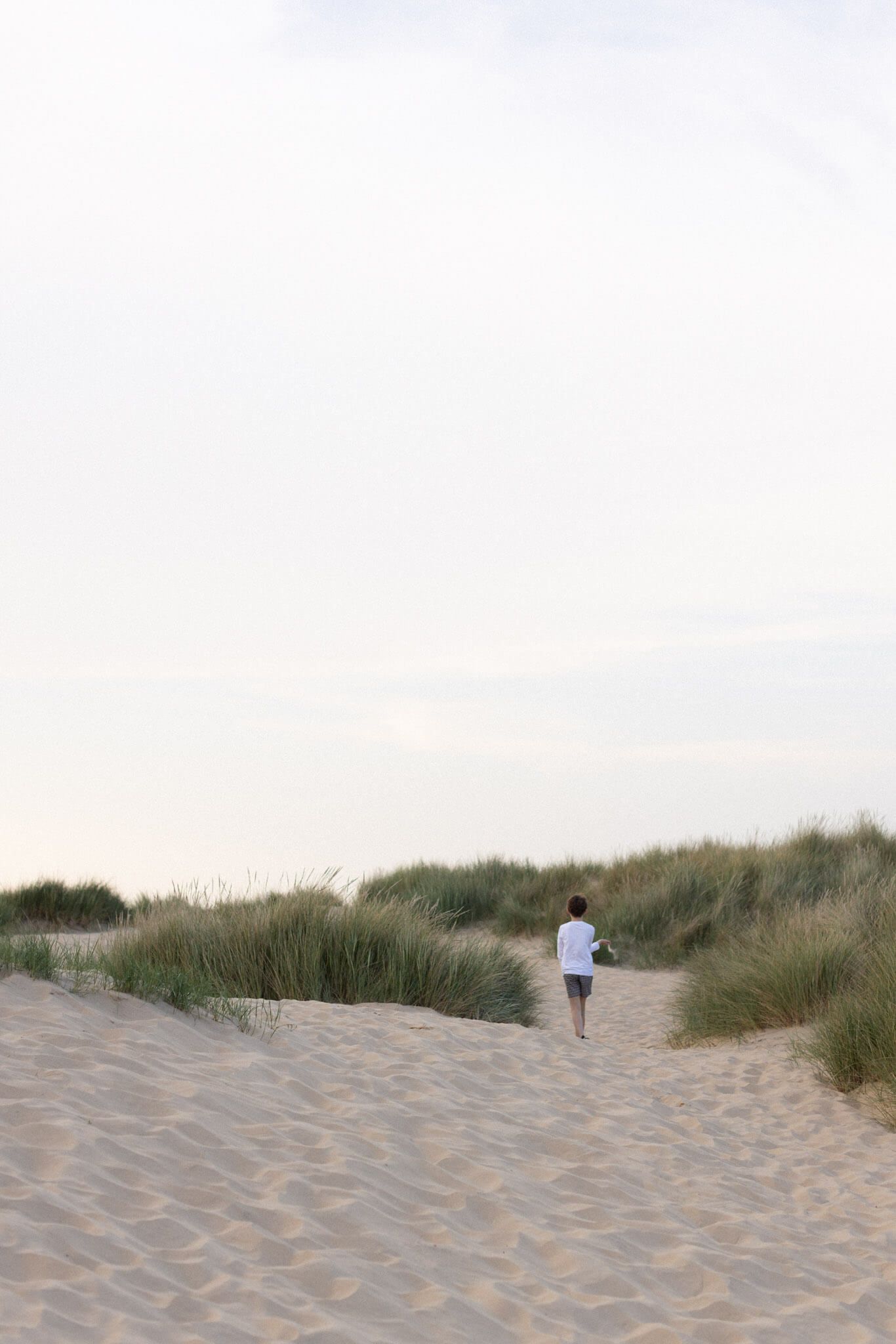 Child walking on sandy dunes with beach grass during an outdoor family photography session