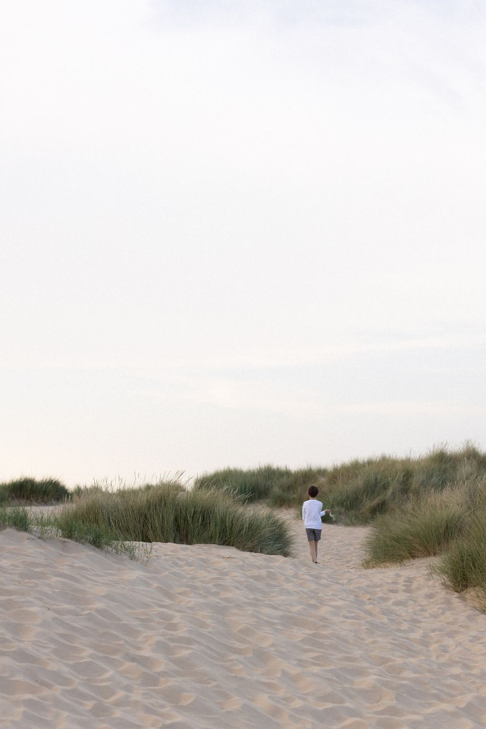 Child walking on sandy dunes with beach grass during an outdoor family photography session