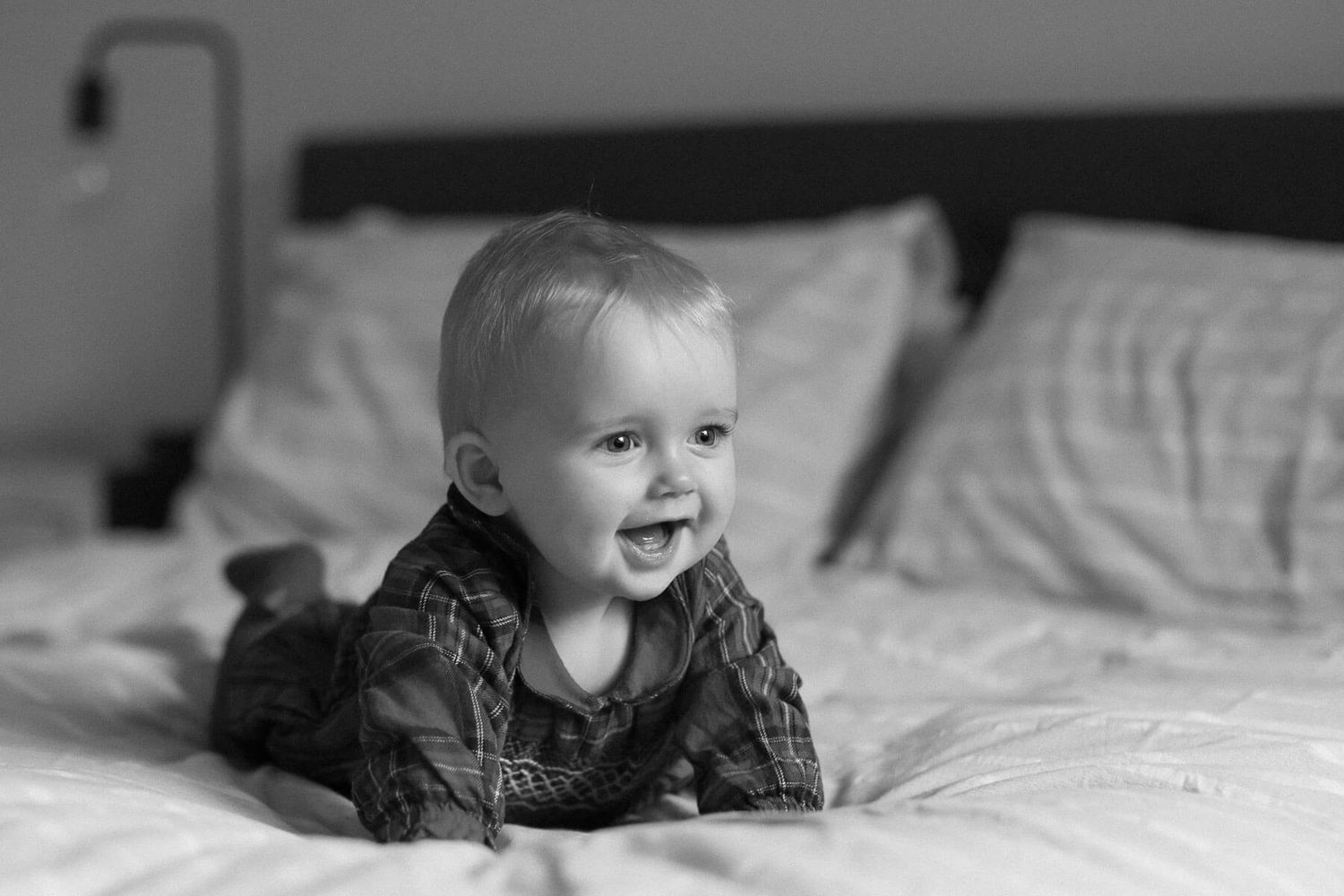 Black and white photo of child crawling on a bed, photographed during an in home family photography session in Brighton