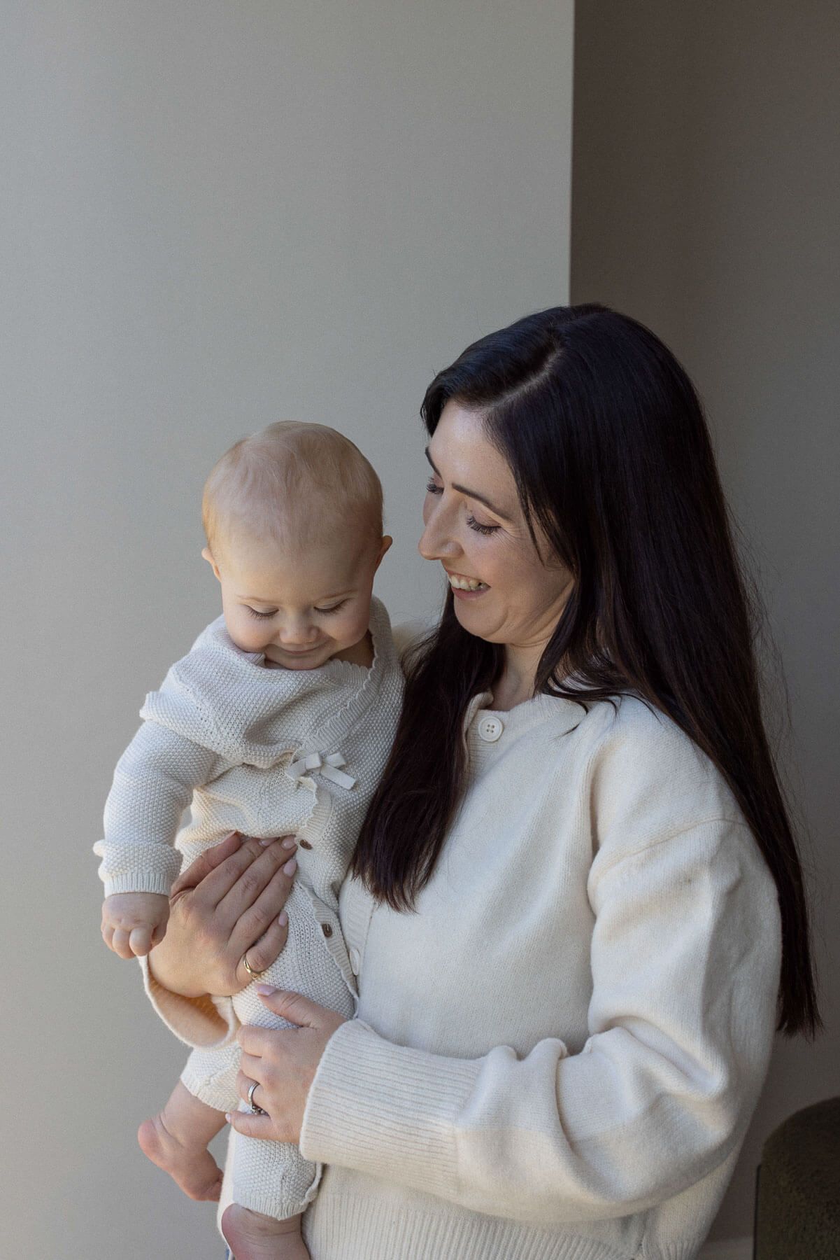 Mother smiling and holding her baby in soft neutral wardrobe tones during a family photography session in Brighton