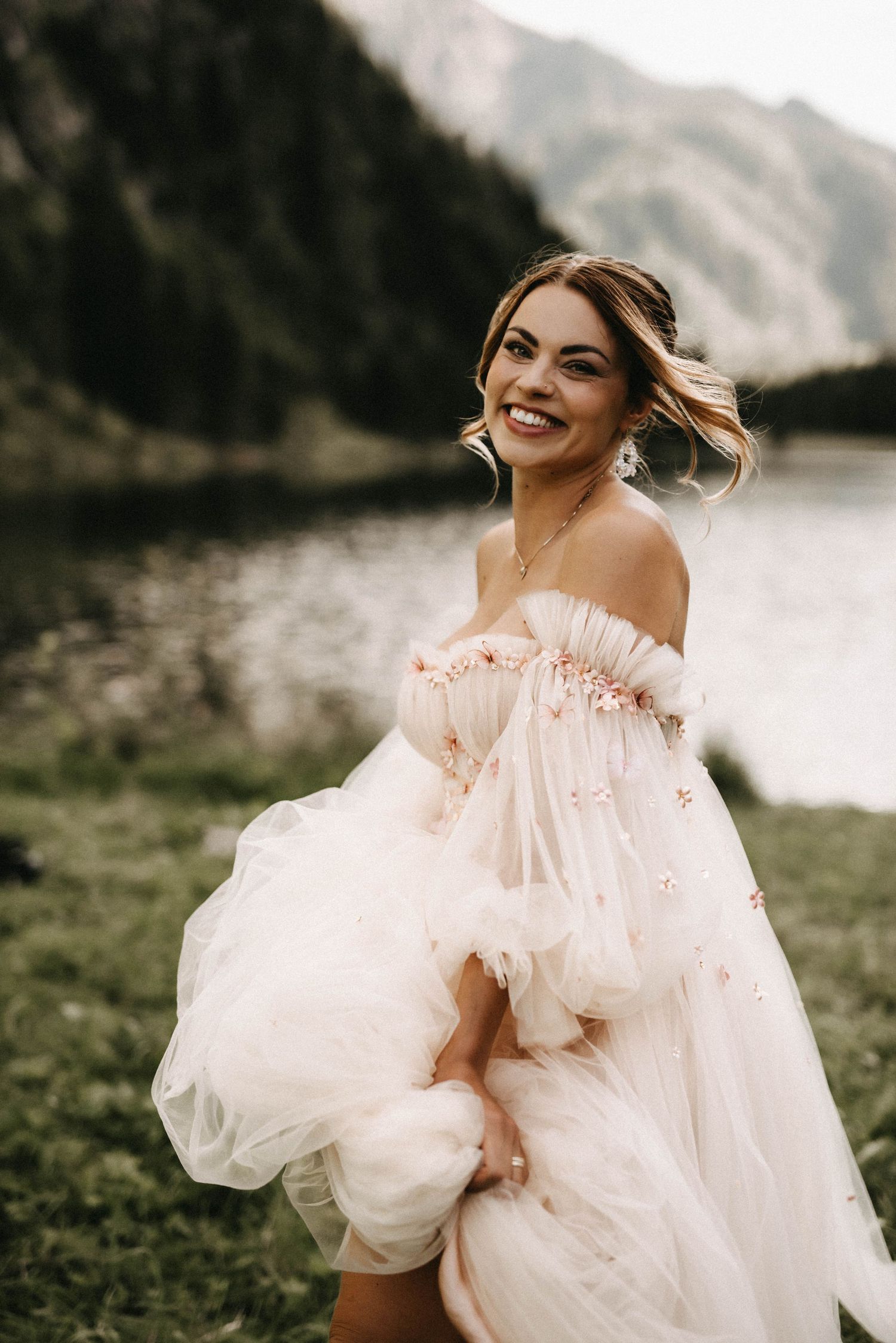 Romantic bridal portrait in flowing tulle dress with puffy sleeves against a mountain lake backdrop.