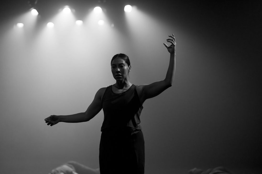 Dancer performs expressive movements under dramatic overhead spotlights.