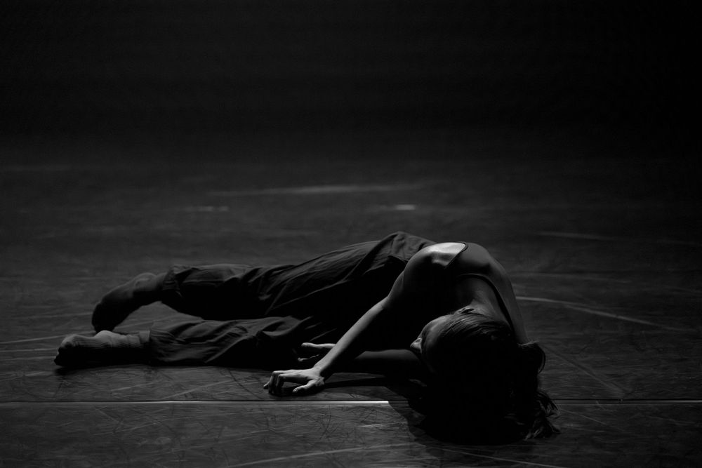 Dancers lying prone on stage floor in artistic black and white composition.