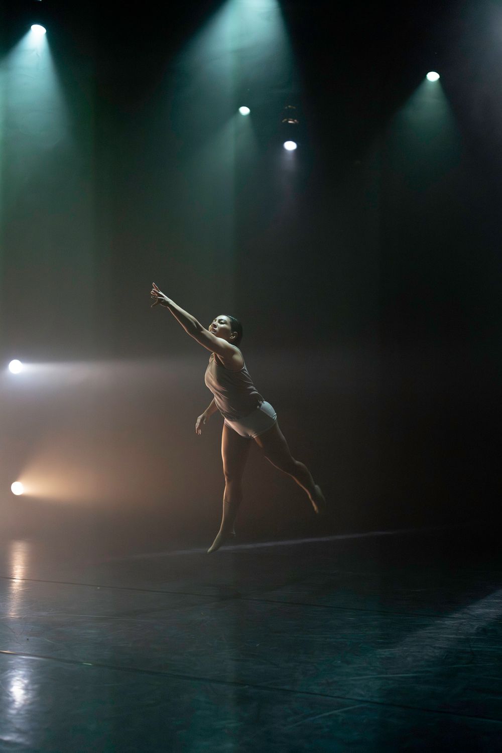 Solo dancer performing expressive movements on a misty, dramatically lit stage.