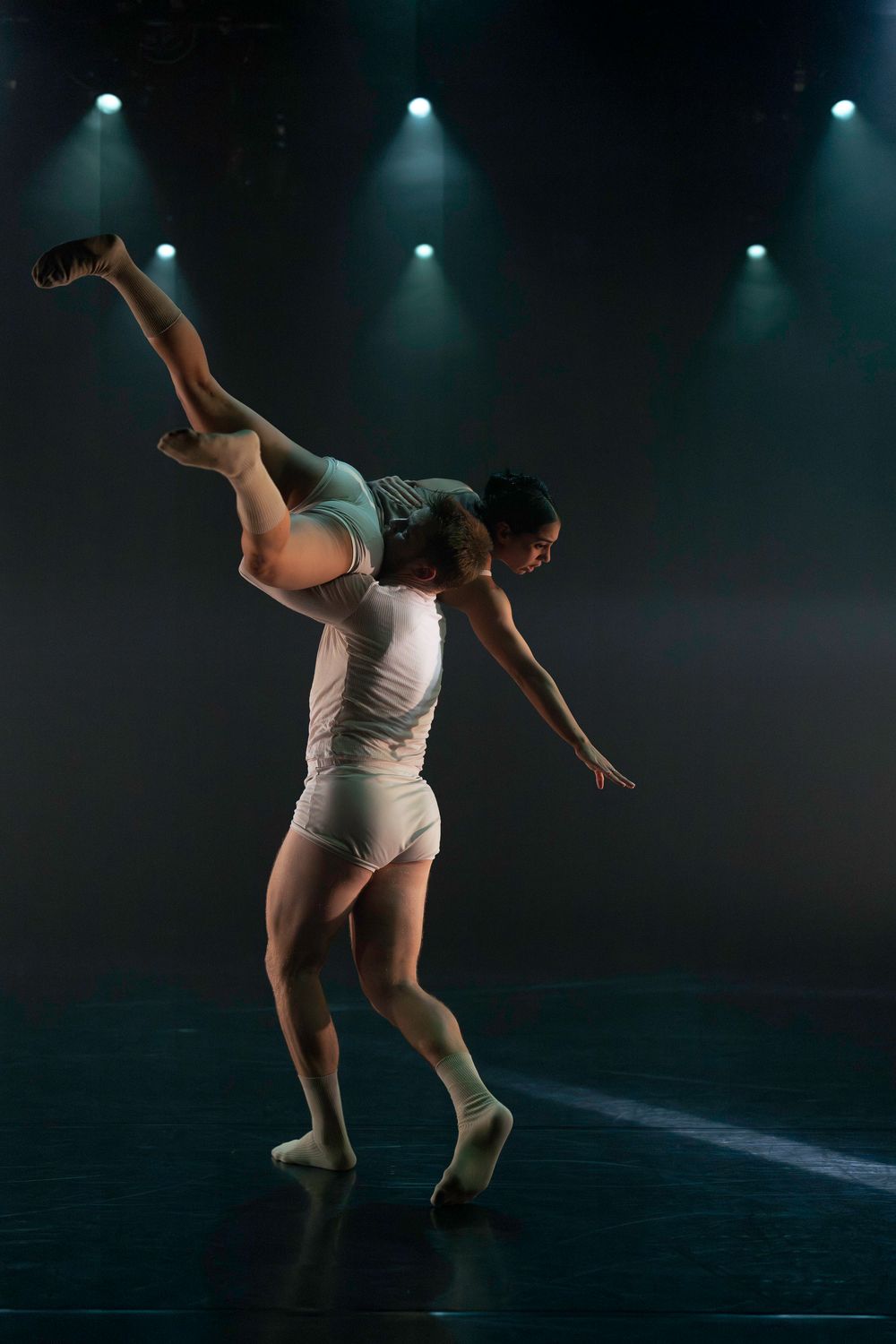Modern dance performance featuring athletic movements under cool blue stage lighting.