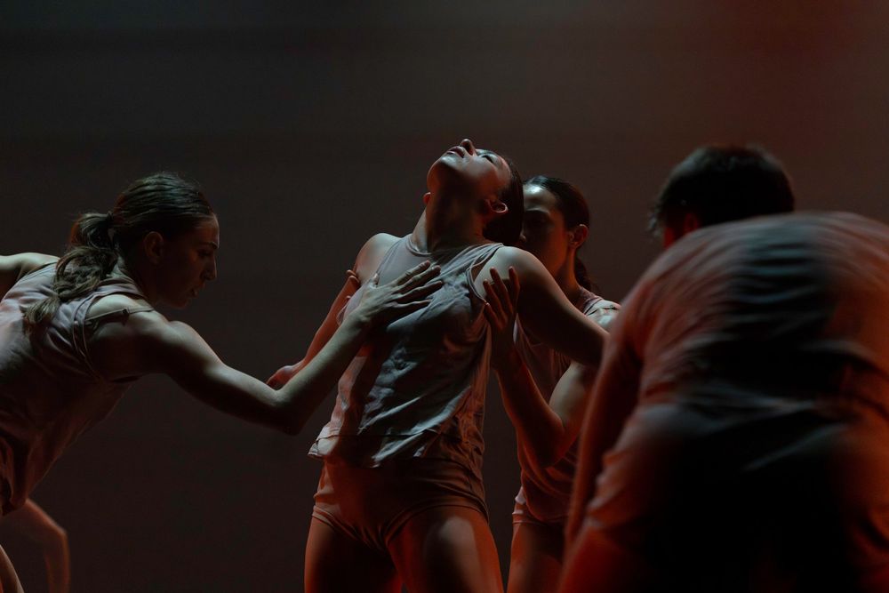 Modern dancers perform an expressive contemporary dance piece in dramatic lighting on a dark stage.