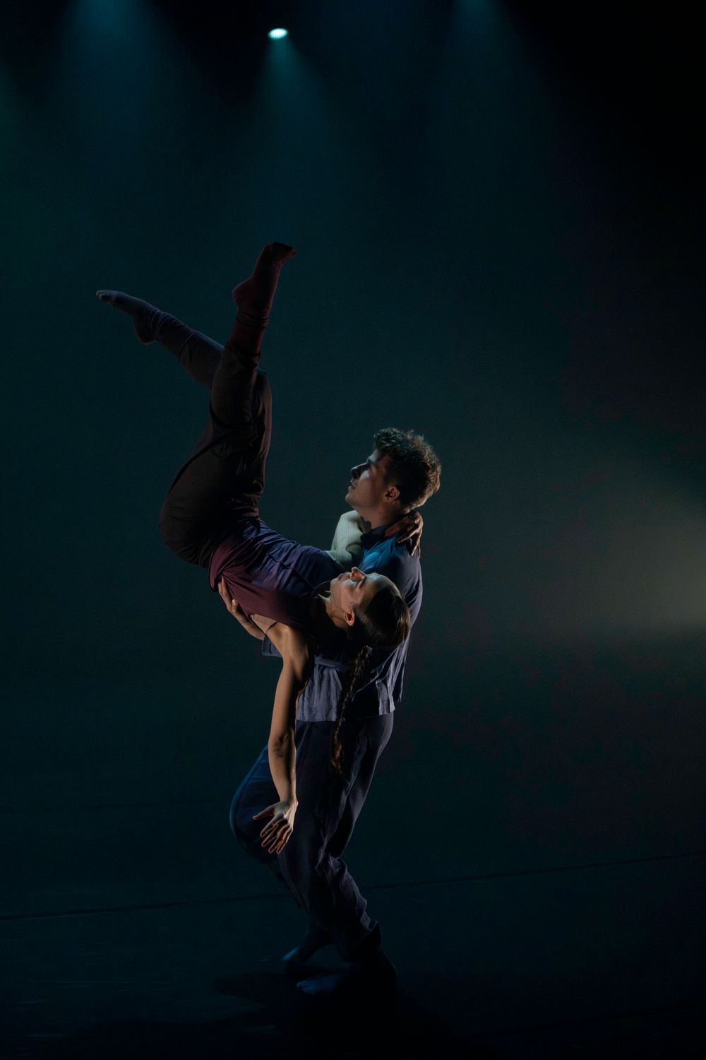 Dancers execute dramatic lifts and partner work against a dark blue-lit stage backdrop.