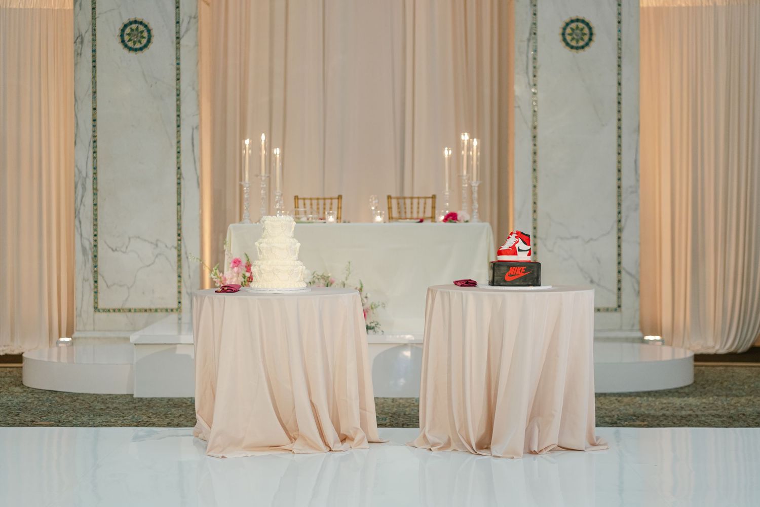 A luxurious ballroom with mint green walls features elegant white curtains and round tables draped in blush linens.