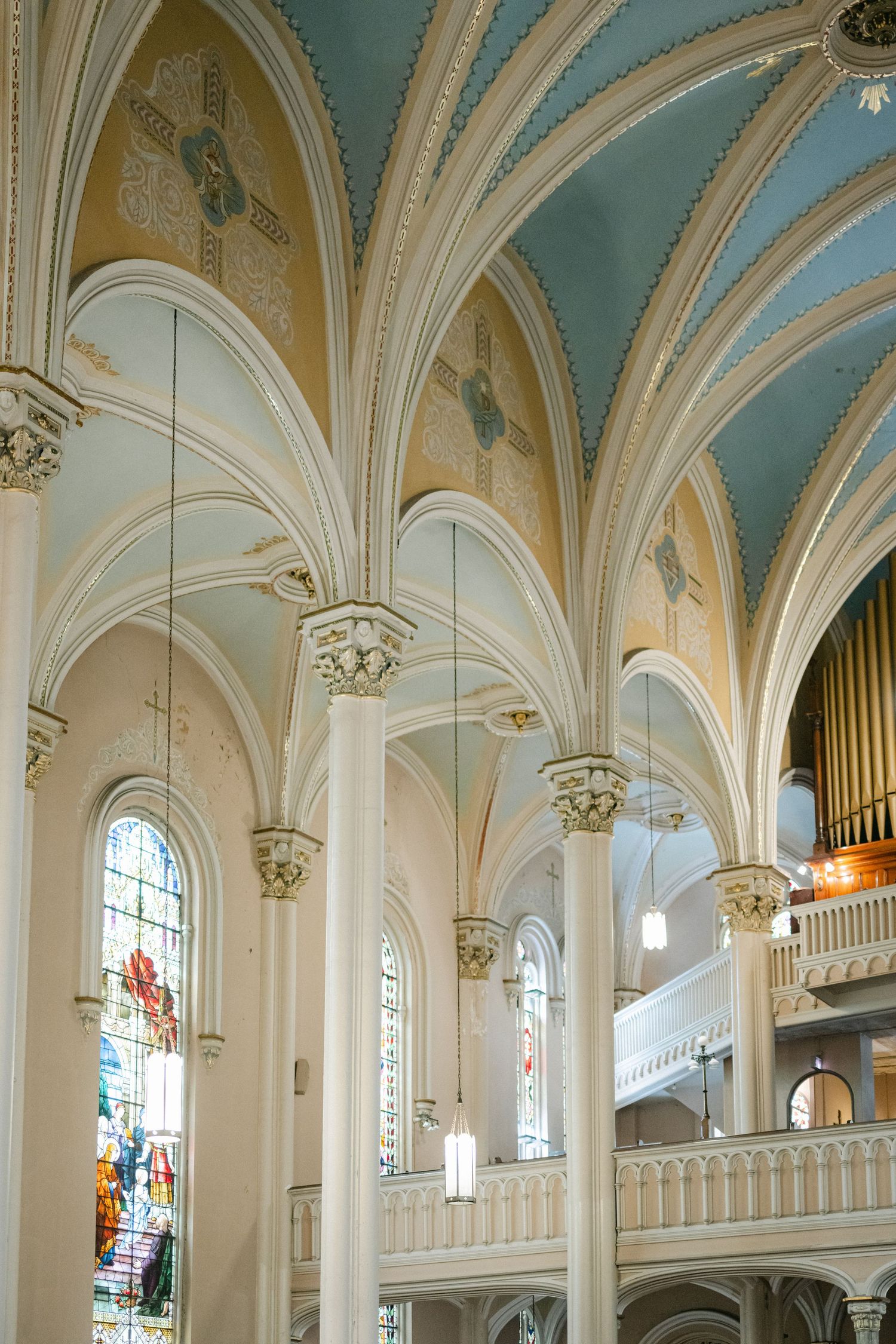Interior view of a Gothic church with vaulted ceilings, white arches, and stained glass windows illuminating the space.