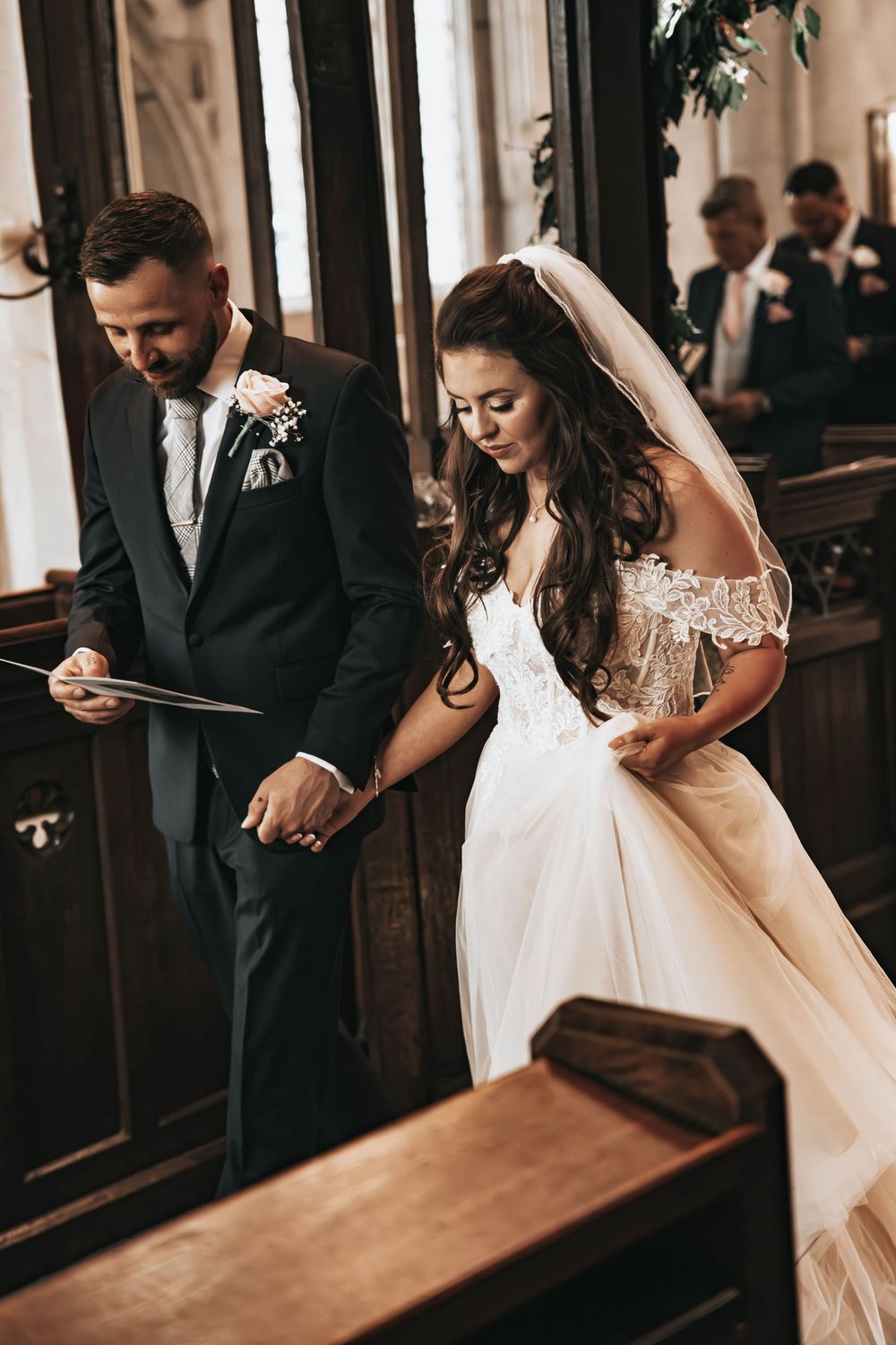 Bride and groom holding hands during a church wedding ceremony, bride wearing a lace veil and off-shoulder gown. Essex Wedding Photographer