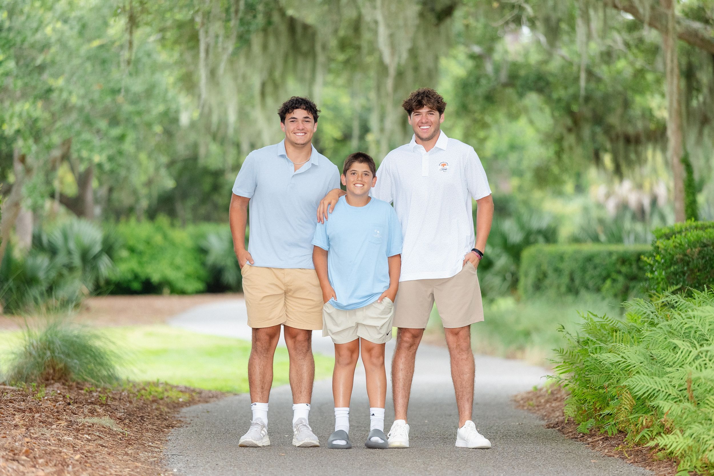 Three brothers posing together on a scenic moss-draped tree-lined path on a sunny day.