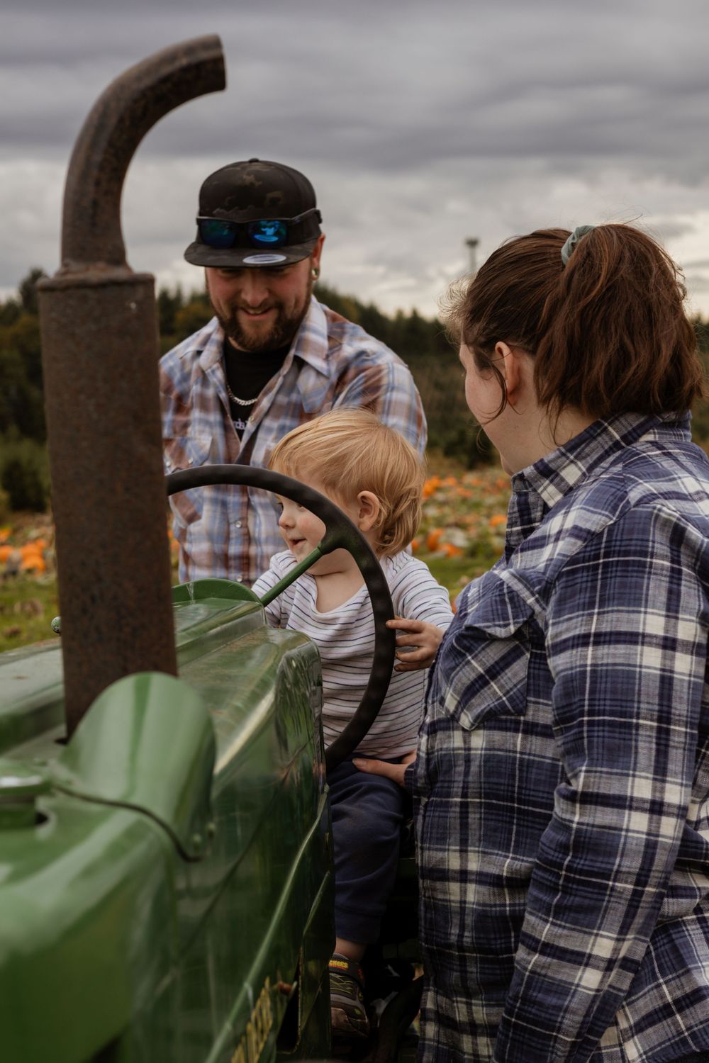 Family of three gathered around a vintage green tractor at a fall pumpkin patch farm.