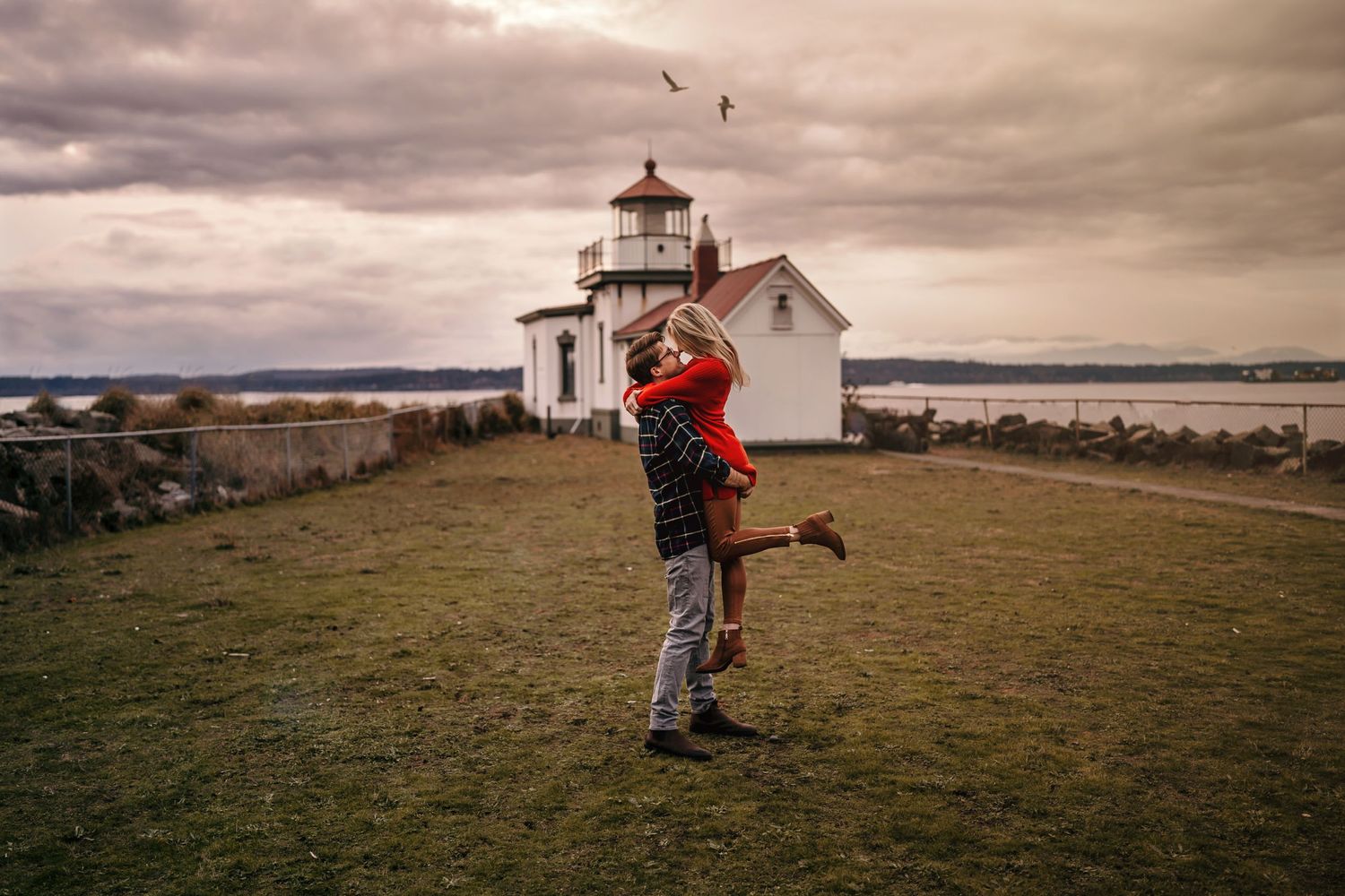 man picking up his fiancé for a kiss at the lighthouse at discovery park