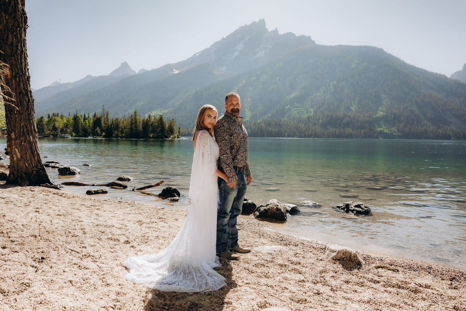A scenic mountain lake surrounded by towering peaks with people enjoying the beach on a sunny summer day.